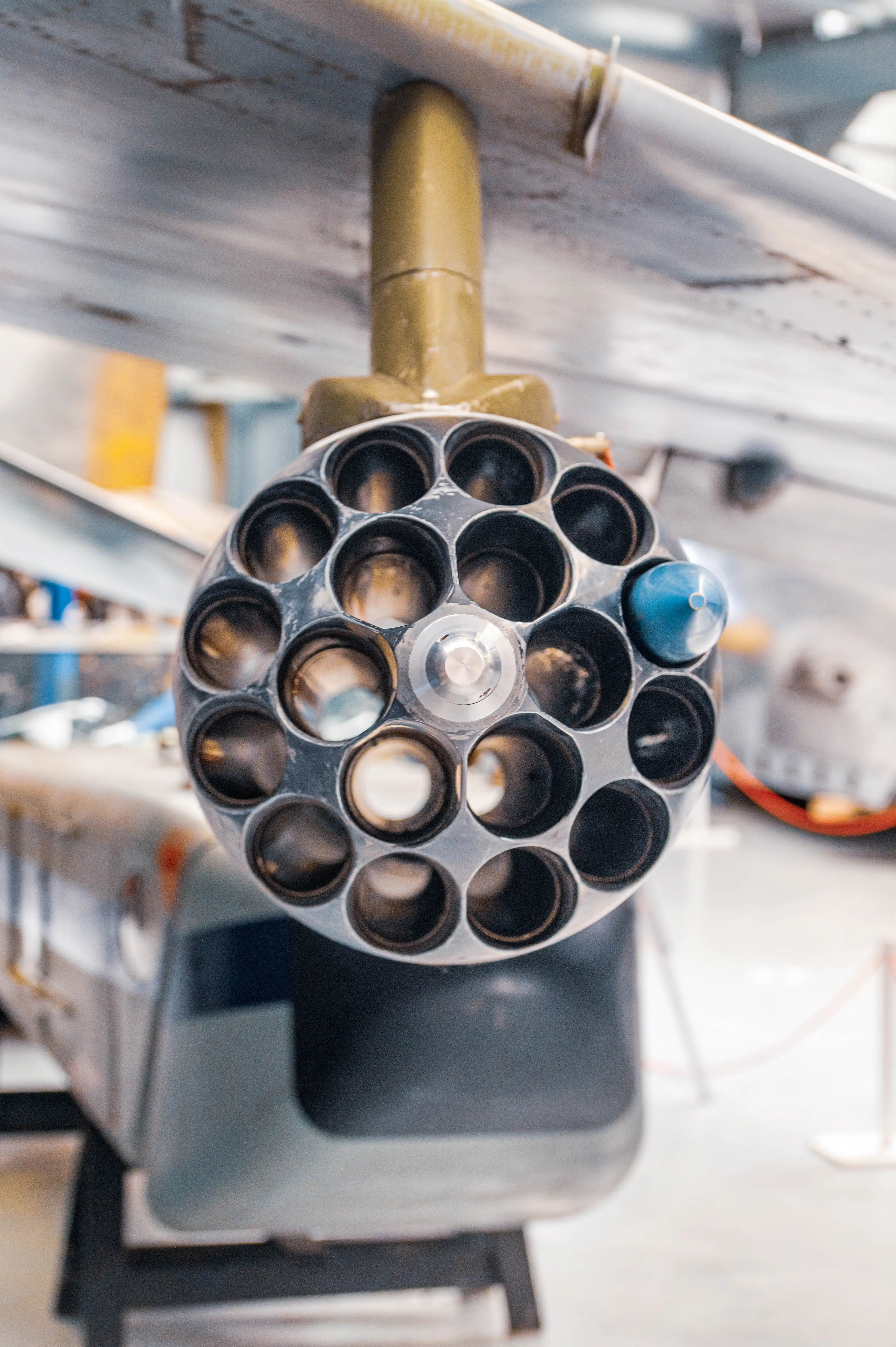 Close-up of a circular rocket pod attached to an aircraft, showing many openings and one blue projectile.