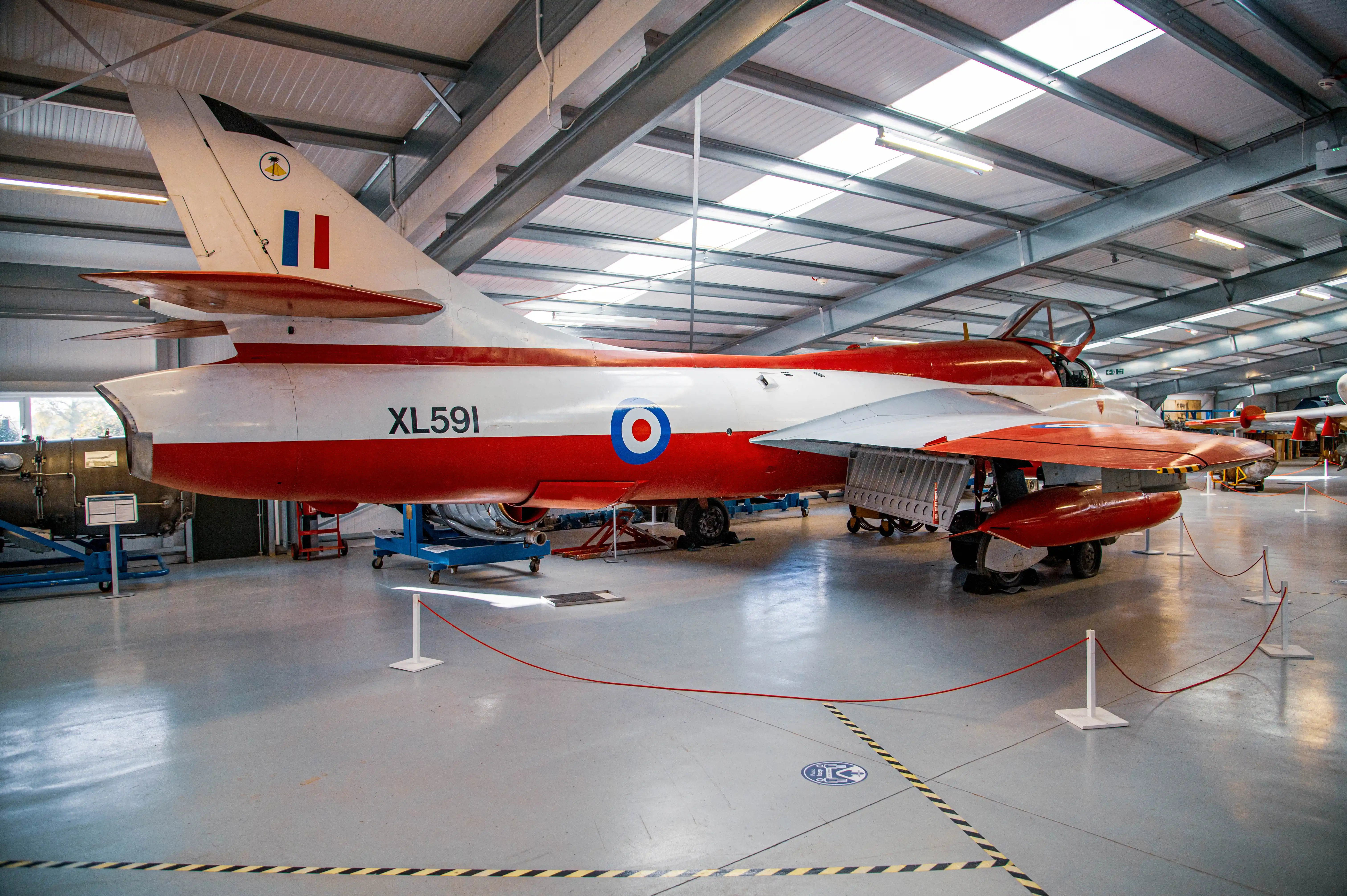 A side view of the Hawker Hunter XL591, painted in red and white with the RAF roundel, parked indoors in an aviation museum.