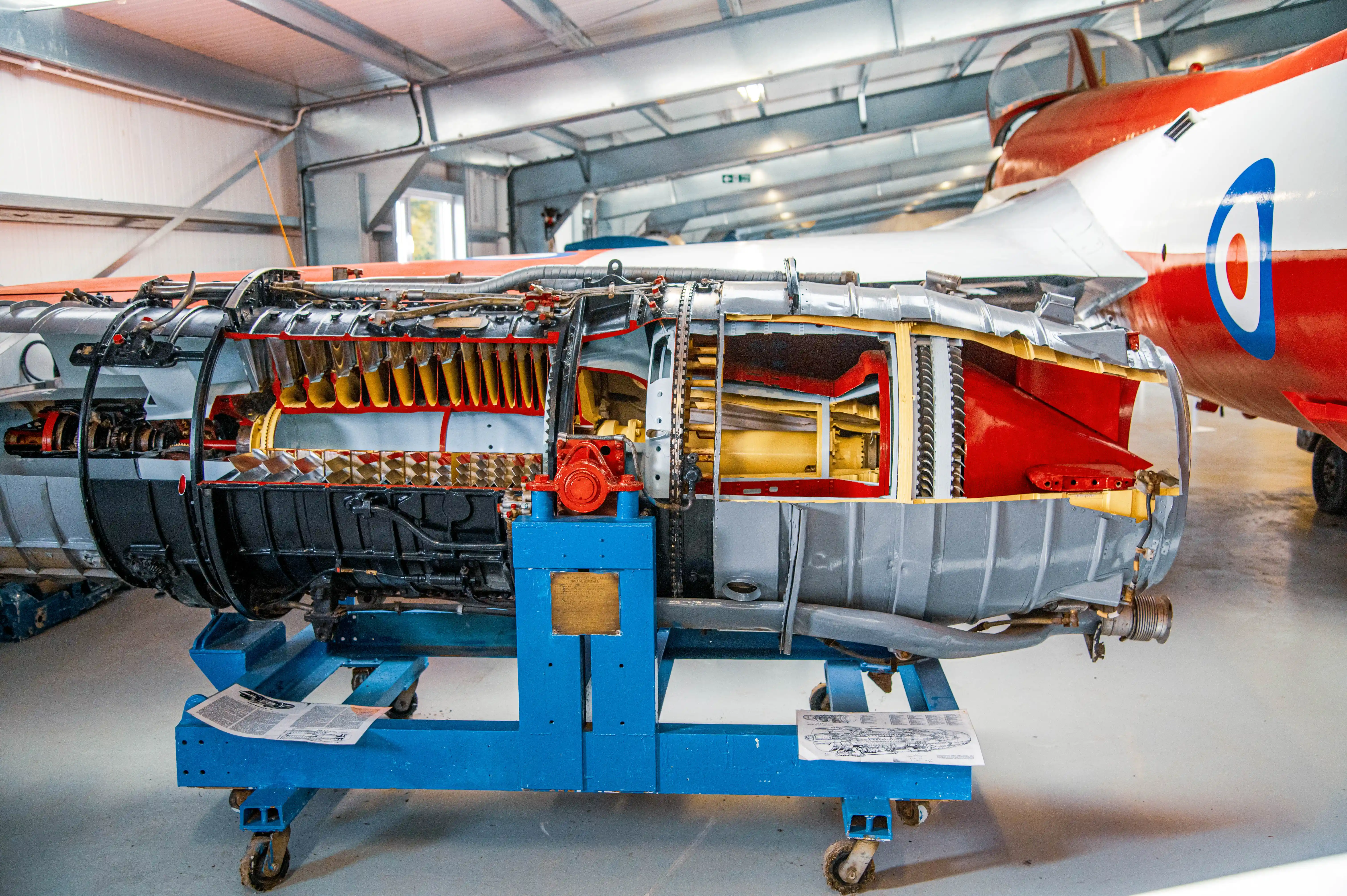 A cutaway view of a jet engine, showcasing its internal mechanics, mounted on a blue trolley in a hangar.