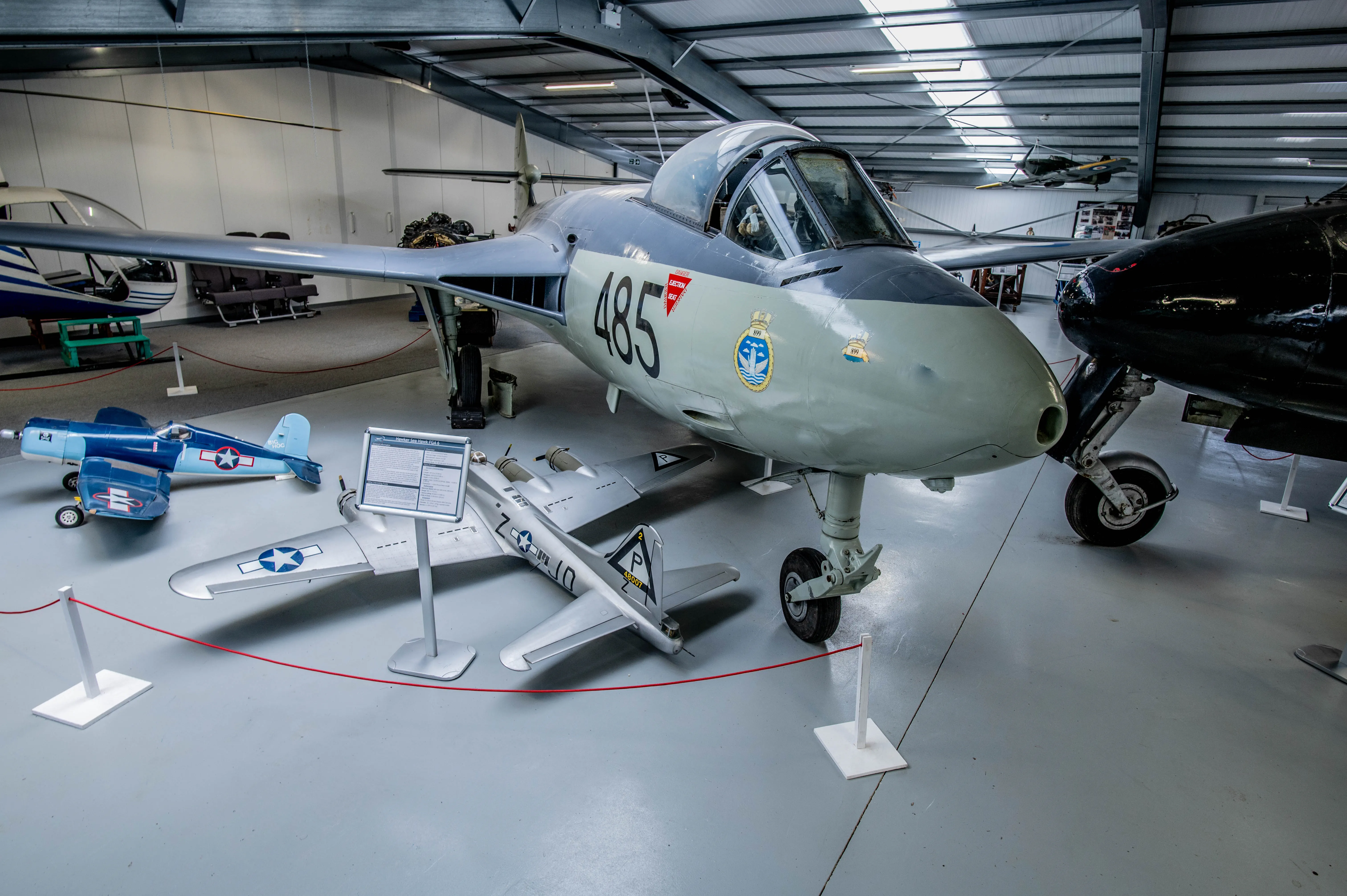 Close-up of jet aircraft with the number 485, in a museum exhibition hall, with a smaller model aircraft in the foreground.