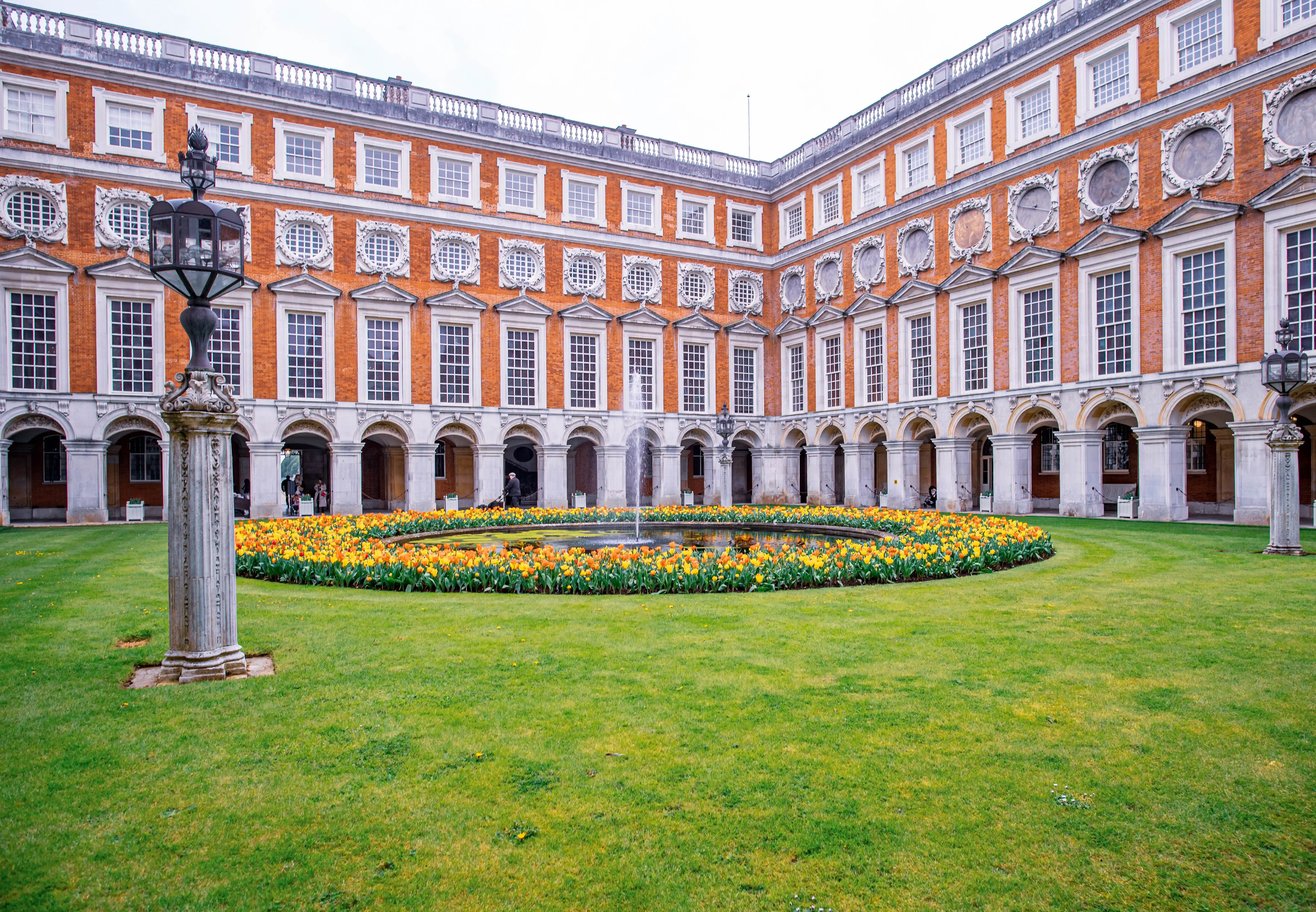 Historic courtyard with central fountain, flower bed, red-brick building and classical architectural details.