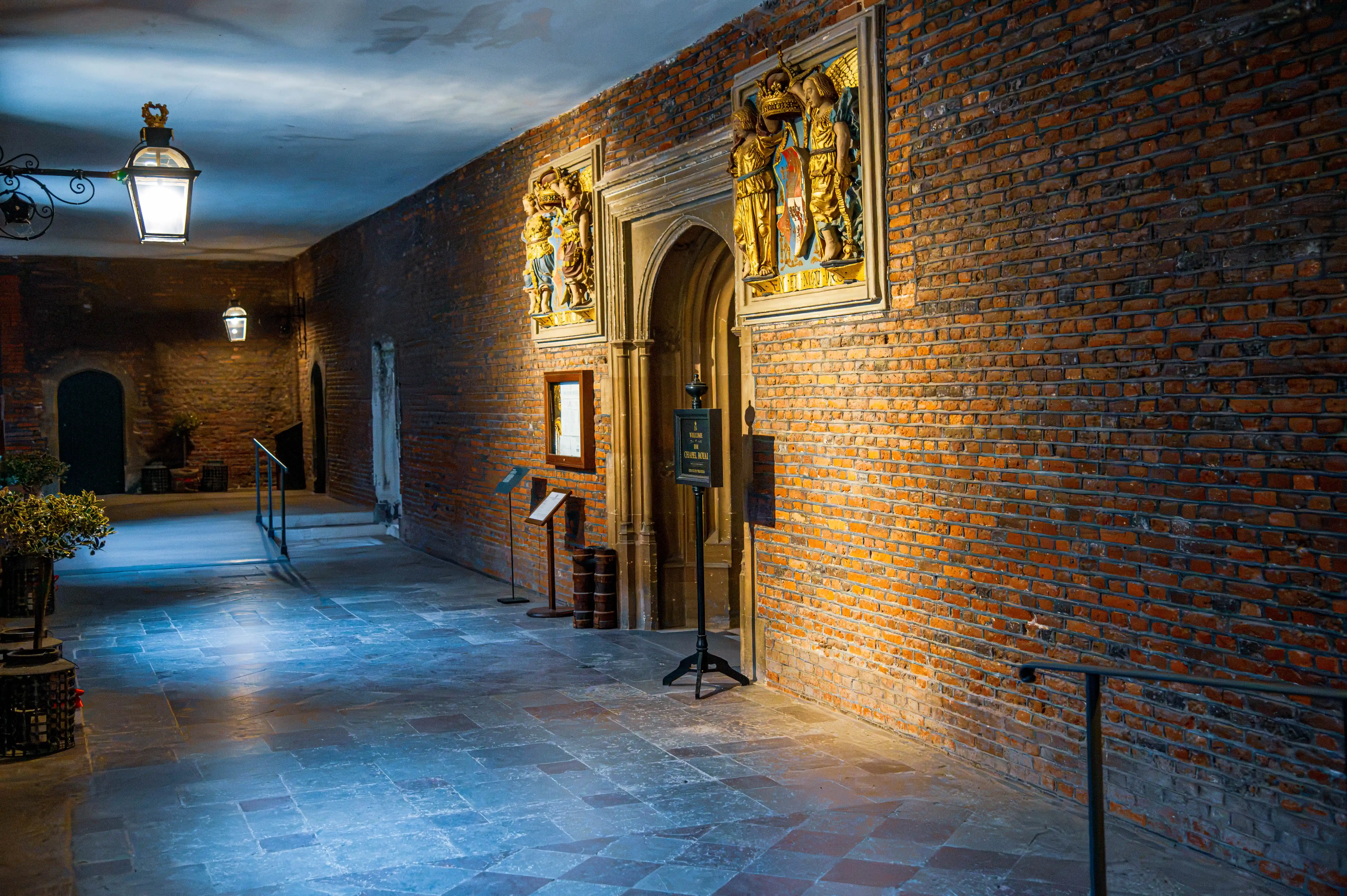 Historic brick corridor with lanterns, arched carved doorway, gilded reliefs and museum plaques.