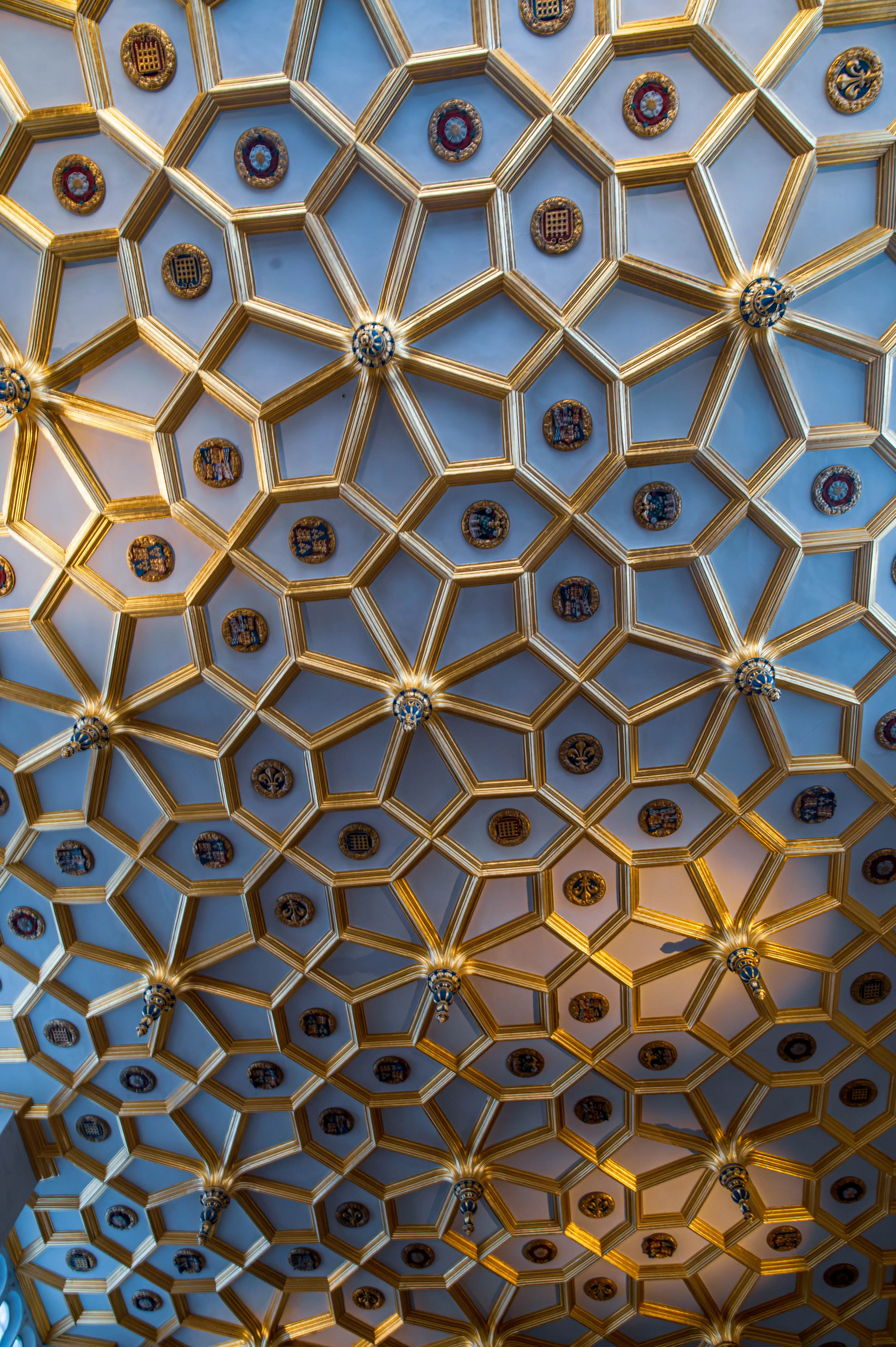 Ornate geometric ceiling with gold-framed polygonal coffers containing heraldic emblems.