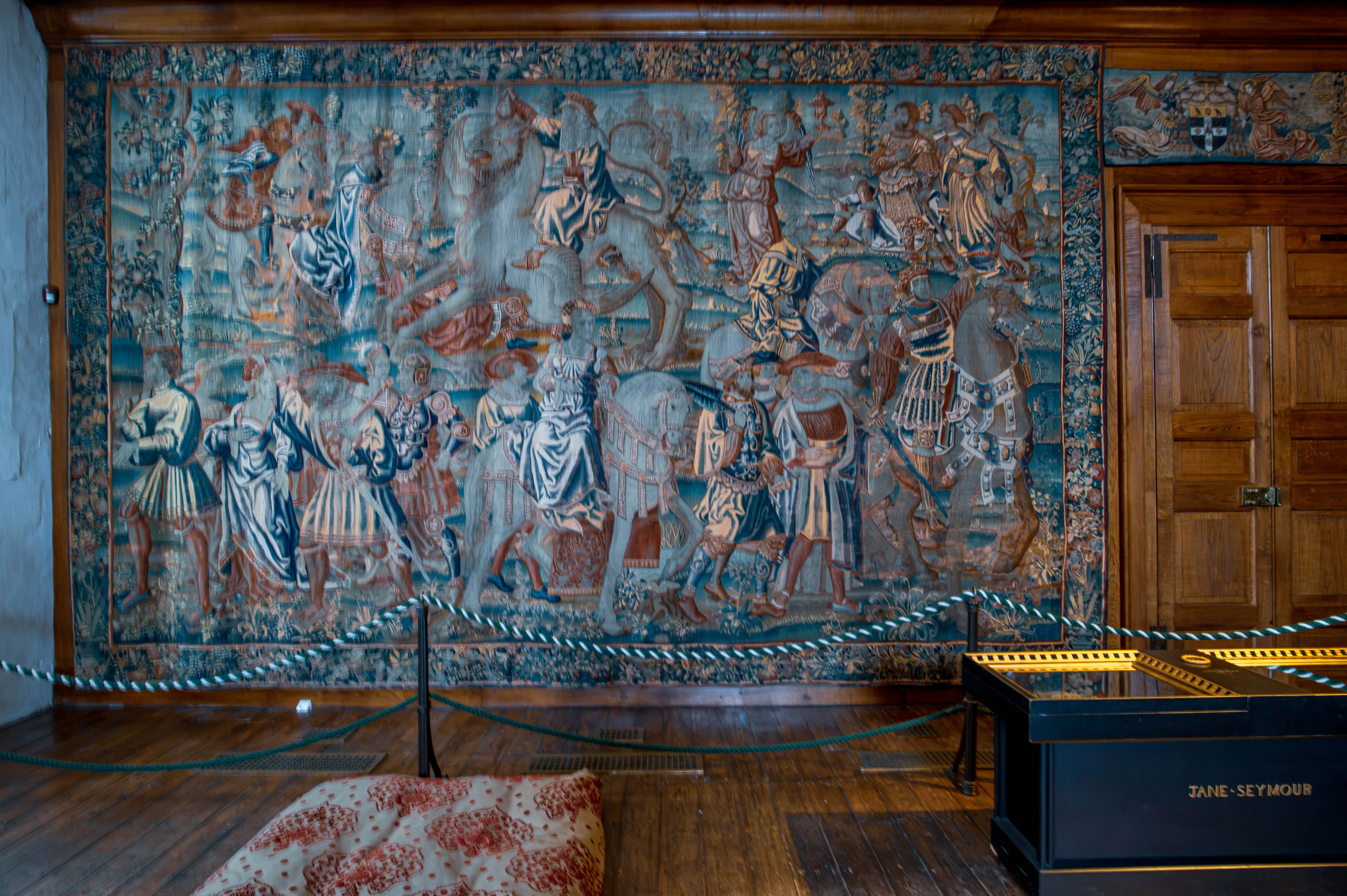 Large historic tapestry showing richly dressed figures, some on horseback, displayed behind a rope barrier with a “Jane Seymour” case in front.