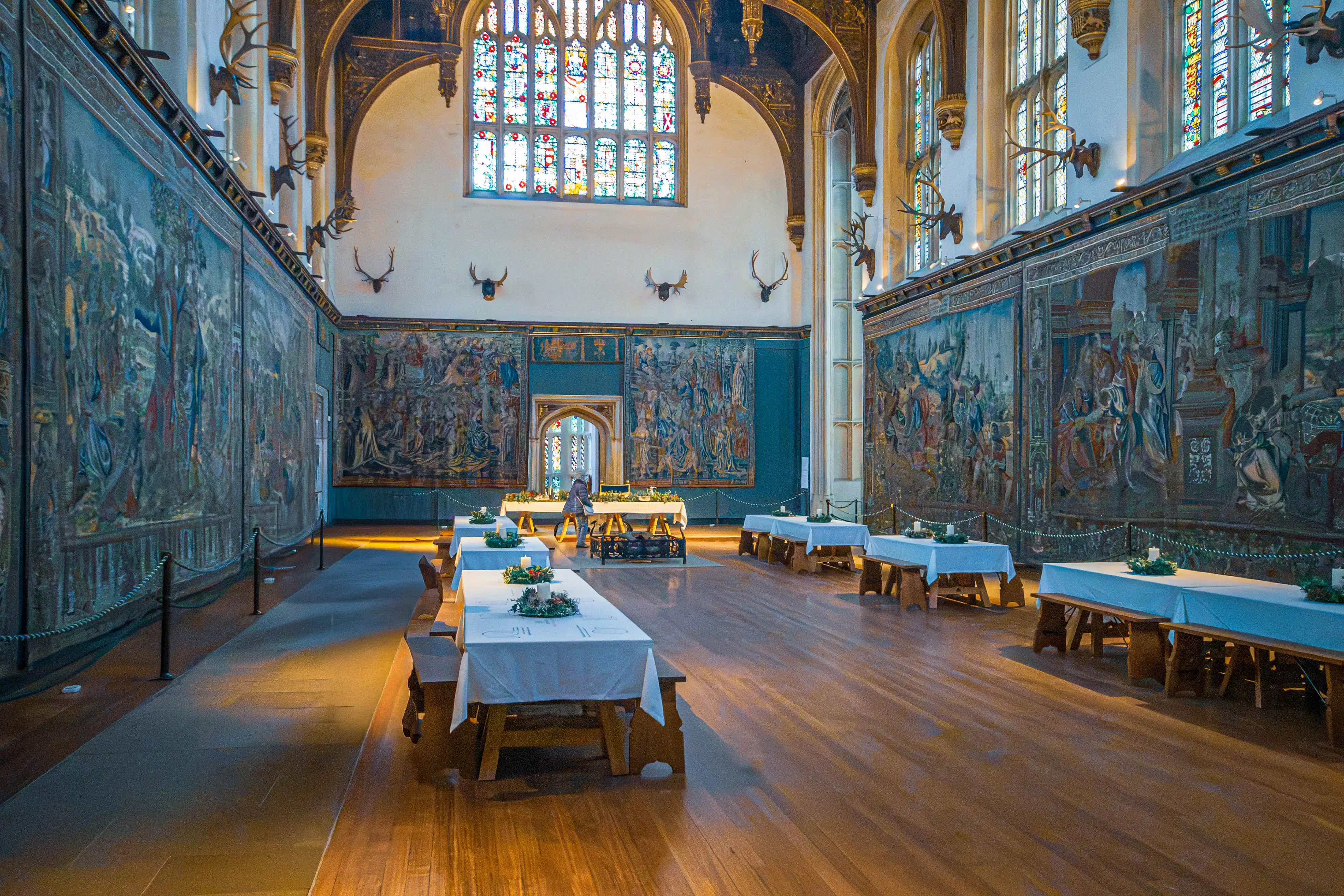 Great hall with vaulted timber ceiling, stained-glass windows, large tapestries, mounted antlers and banquet tables with floral centrepieces.