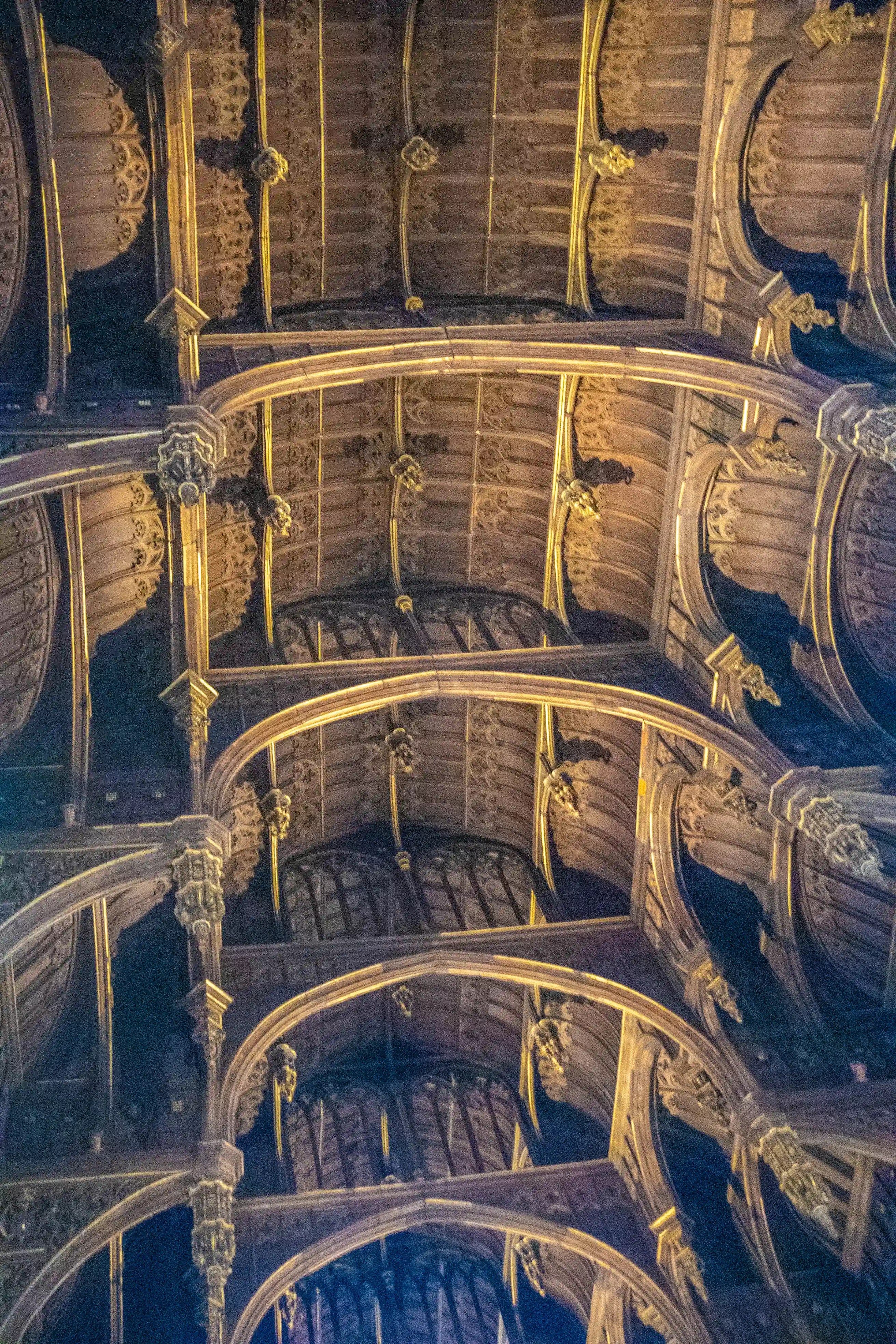 Carved timber ceiling with ribbed arches, tracery and sculpted bosses highlighted by warm lighting.