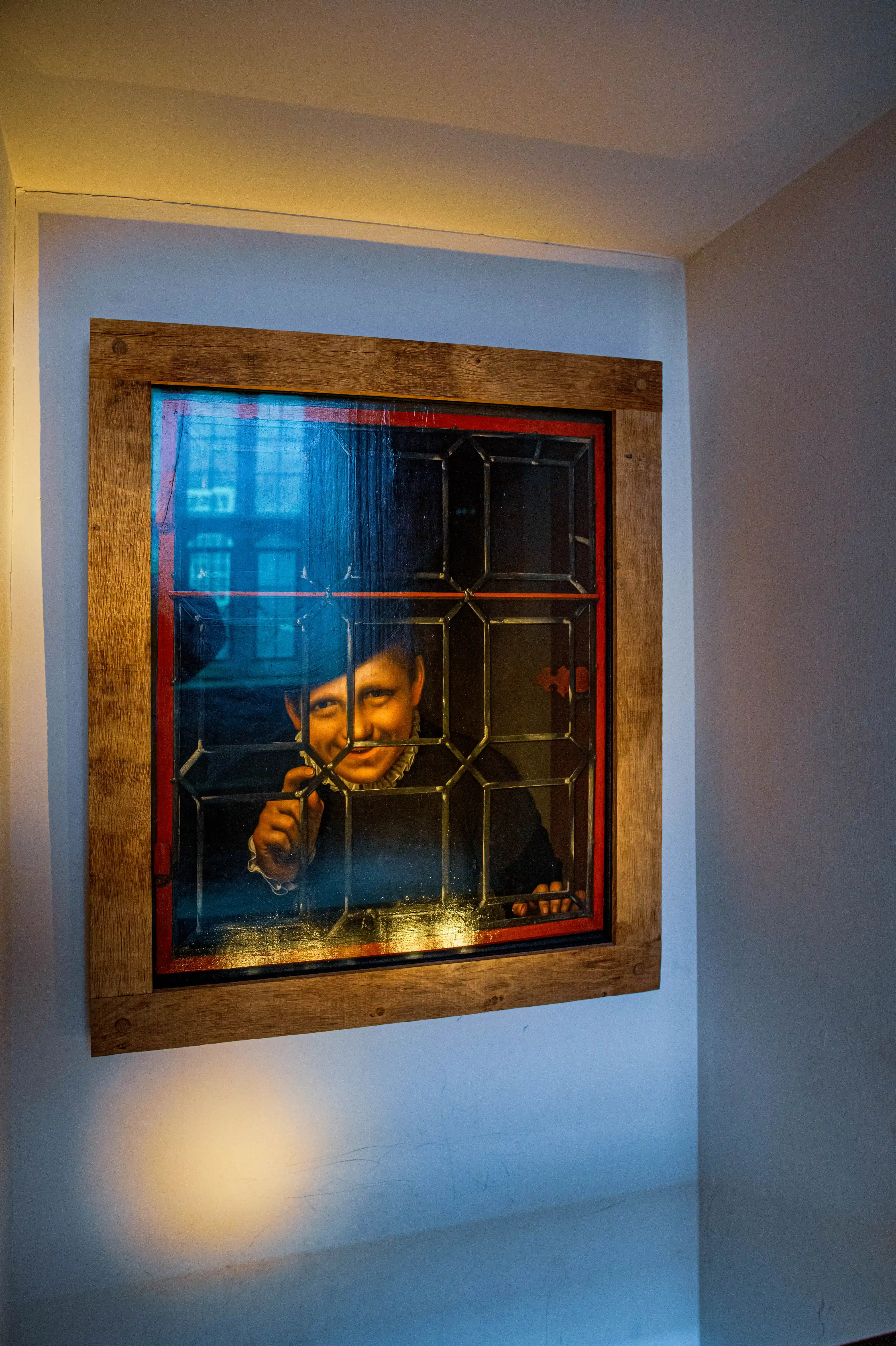 Framed artwork of a figure looking through a leaded-glass window, displayed on a cool-toned wall.