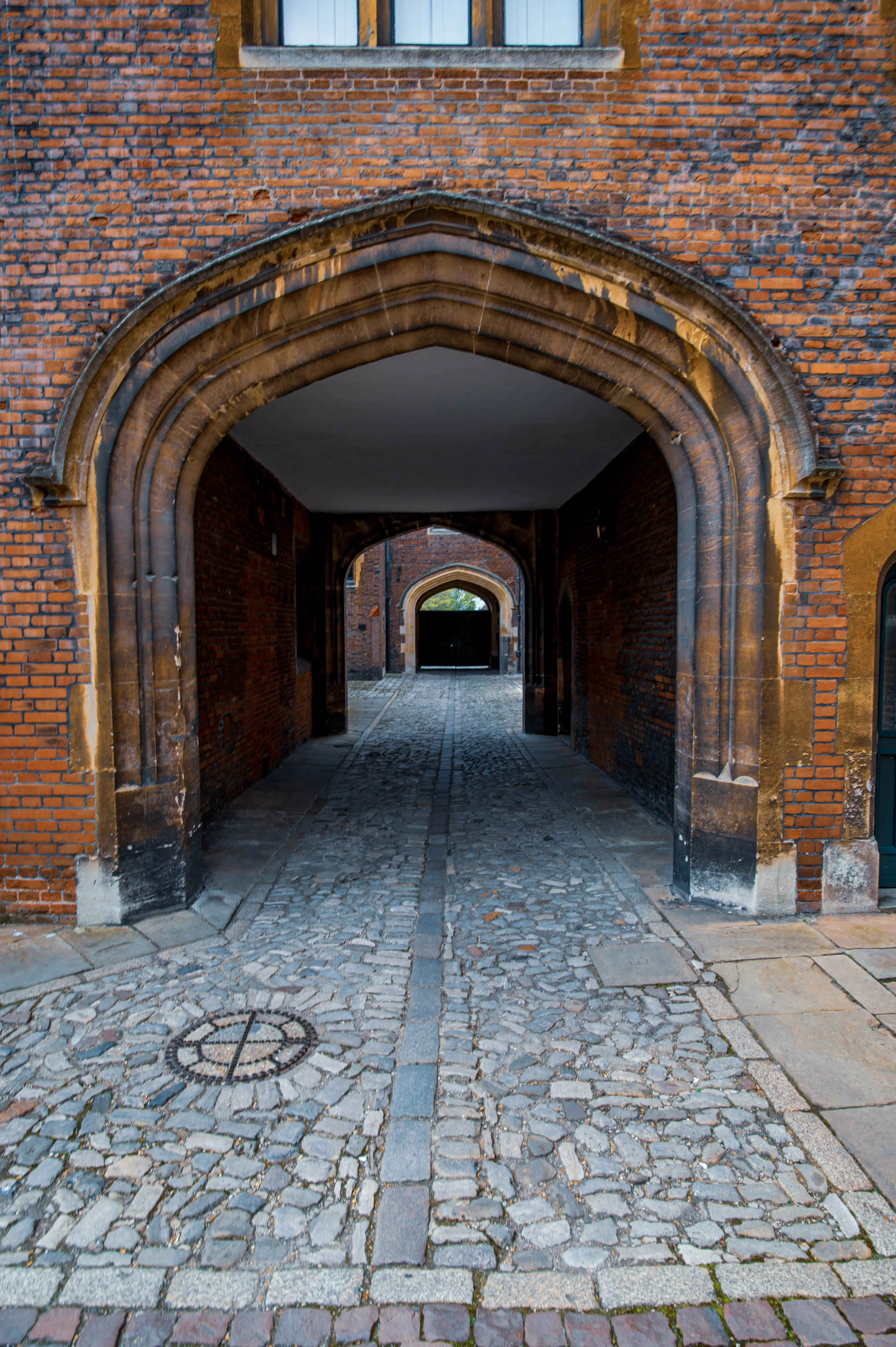 Brick passage with pointed Gothic arches, cobblestones, stone borders and a small window above the arch.
