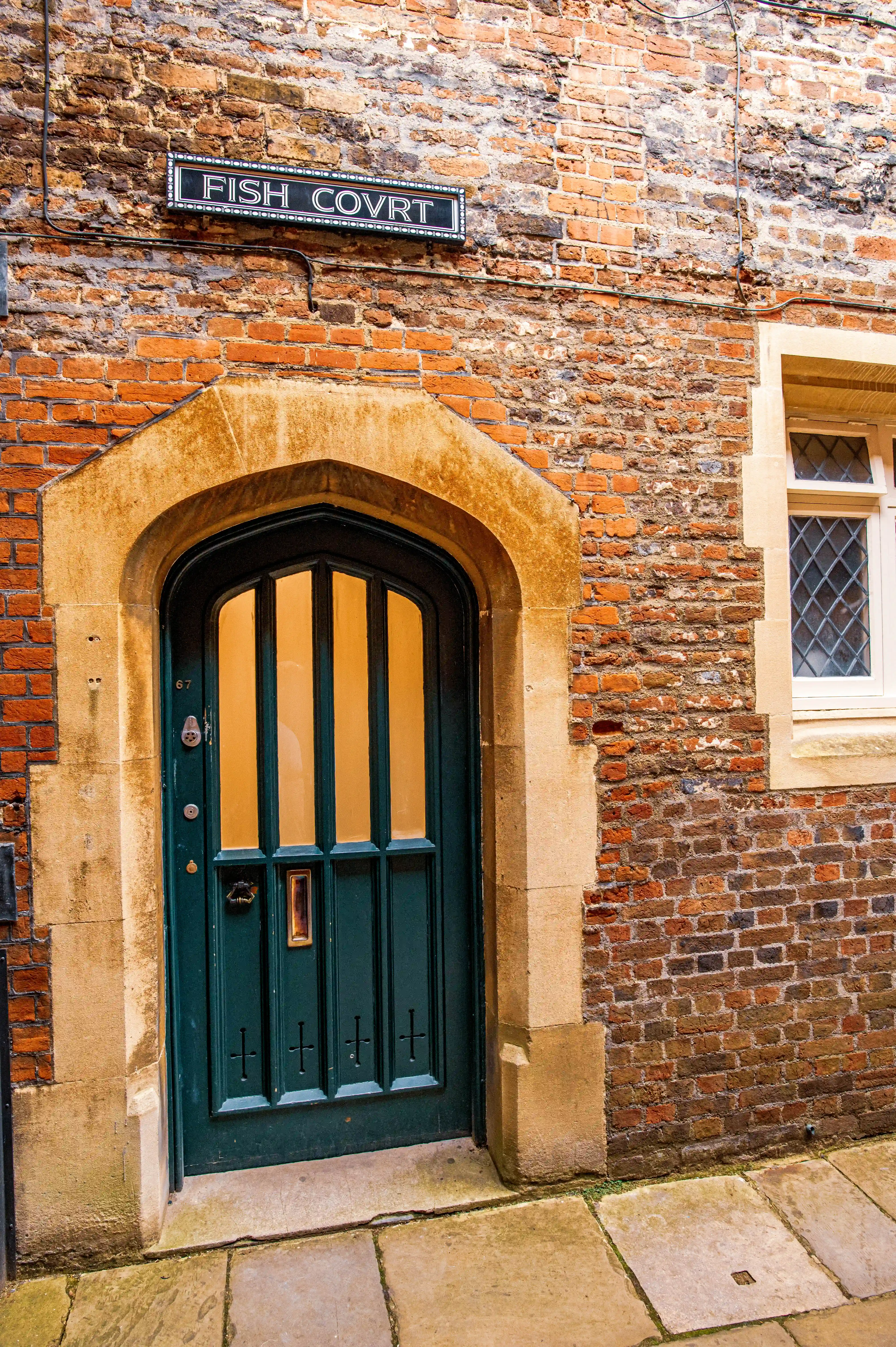 Brick building with arched green door, “FISH COVRT” sign and diamond-patterned leaded window