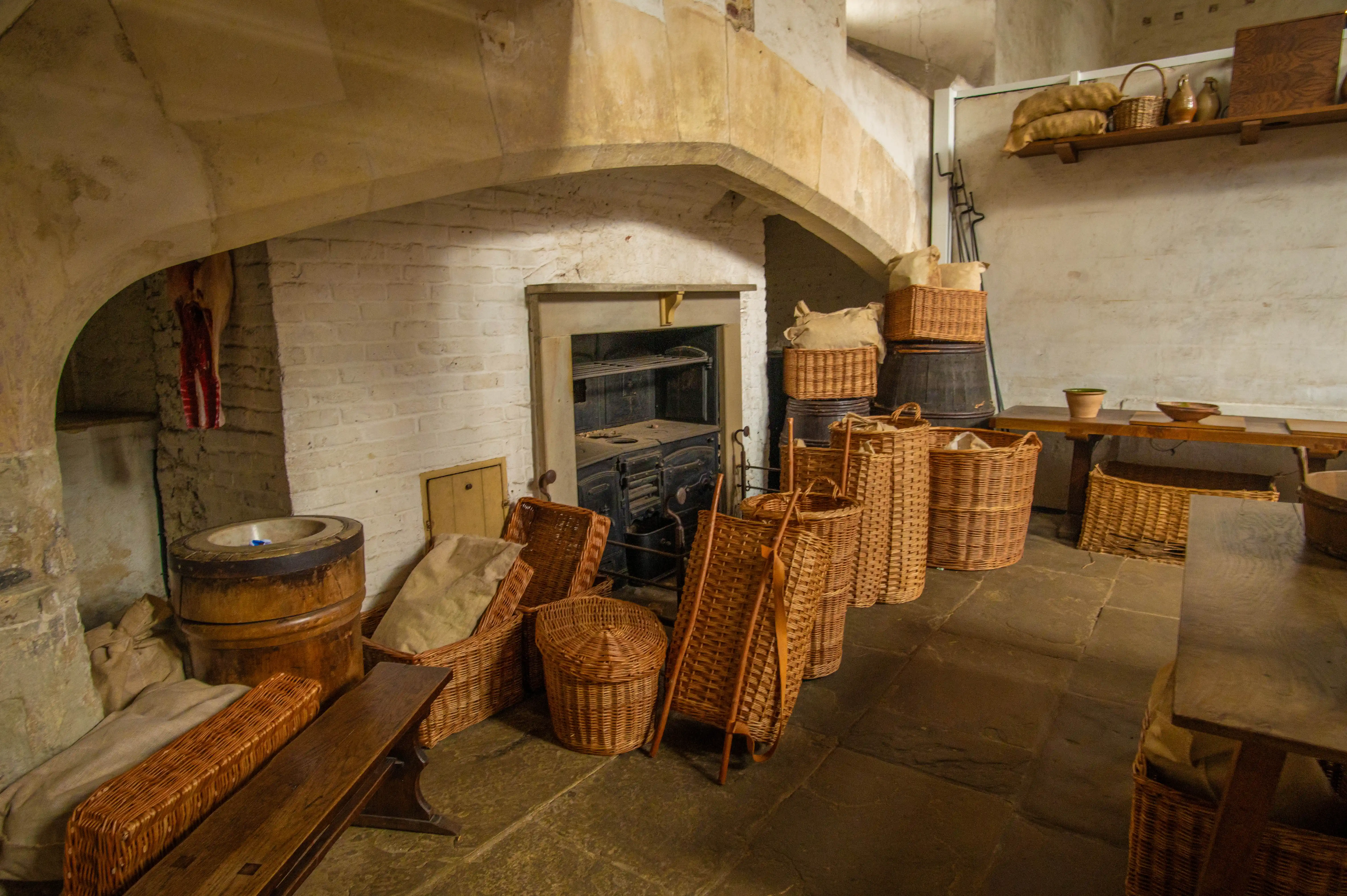 Historic kitchen with stone hearth, wicker baskets, barrels, pottery and whitewashed brick walls.