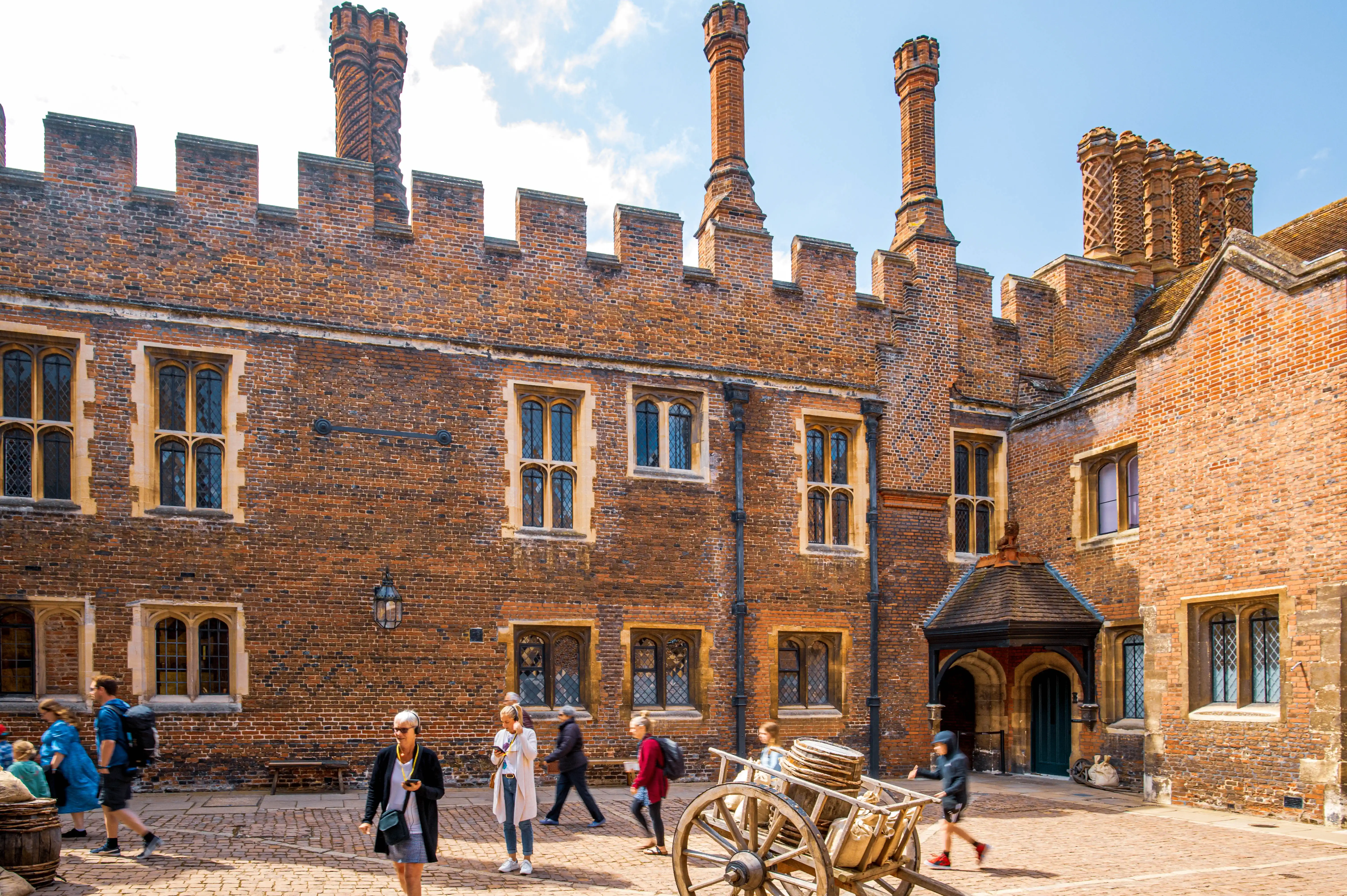 Tudor courtyard with ornate chimneys, crenellated parapets, tall leaded windows and a wooden cart.