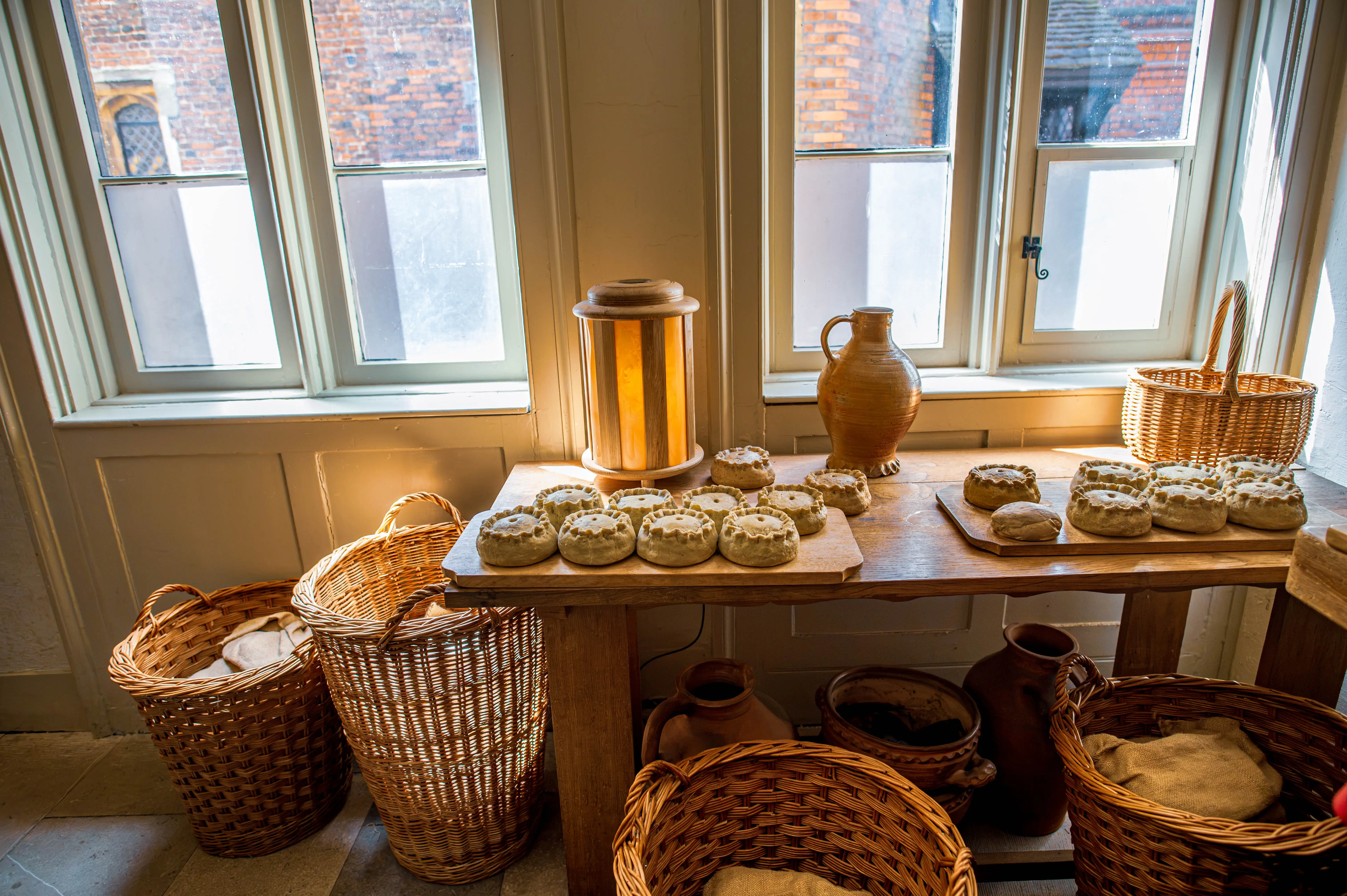 Rustic bread-making scene with wooden table, round loaves, wicker baskets and window light.