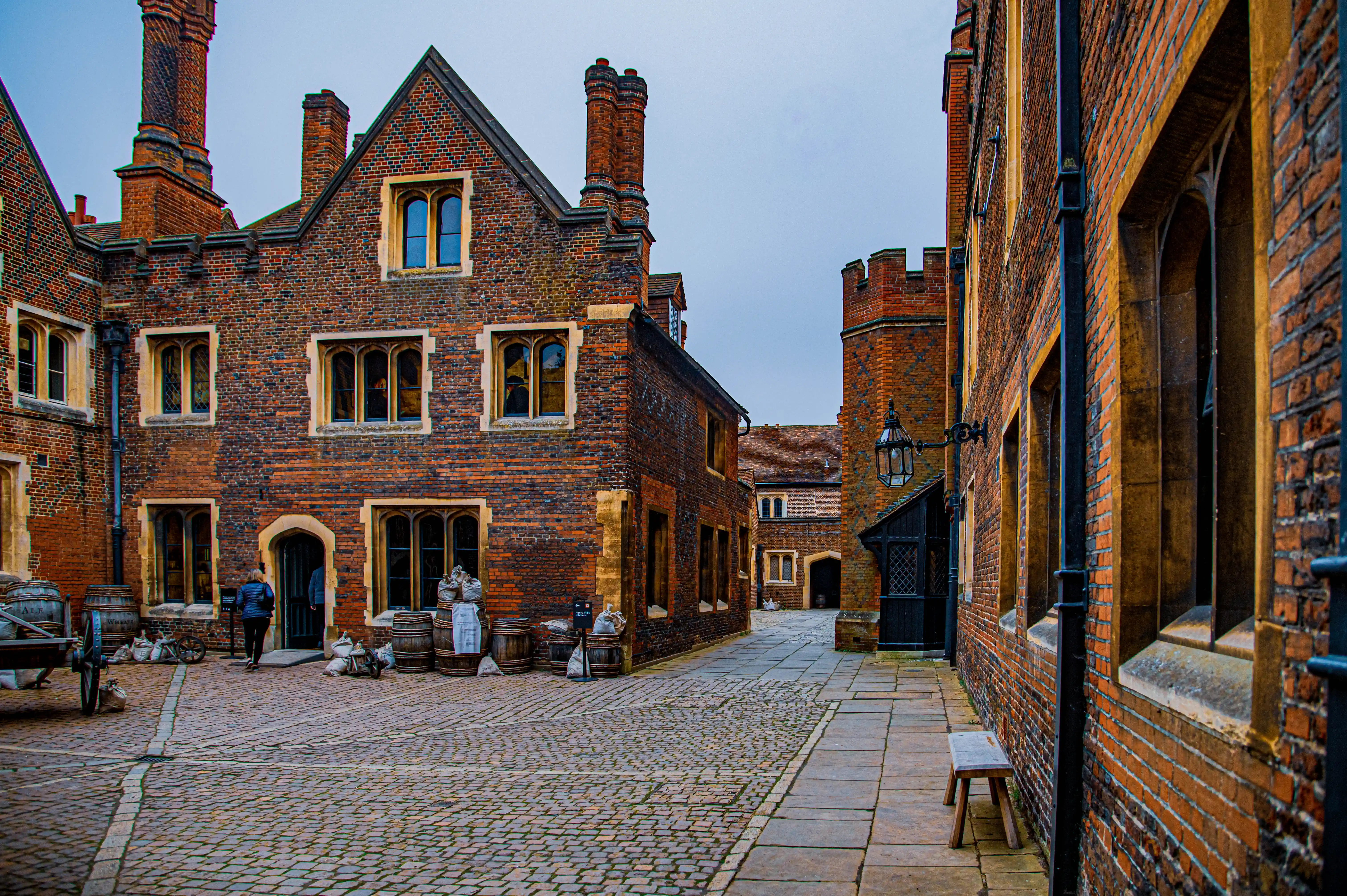 Historic brick courtyard with Gothic windows, decorative chimneys, crenellated parapets, barrels, sacks and wooden cart.