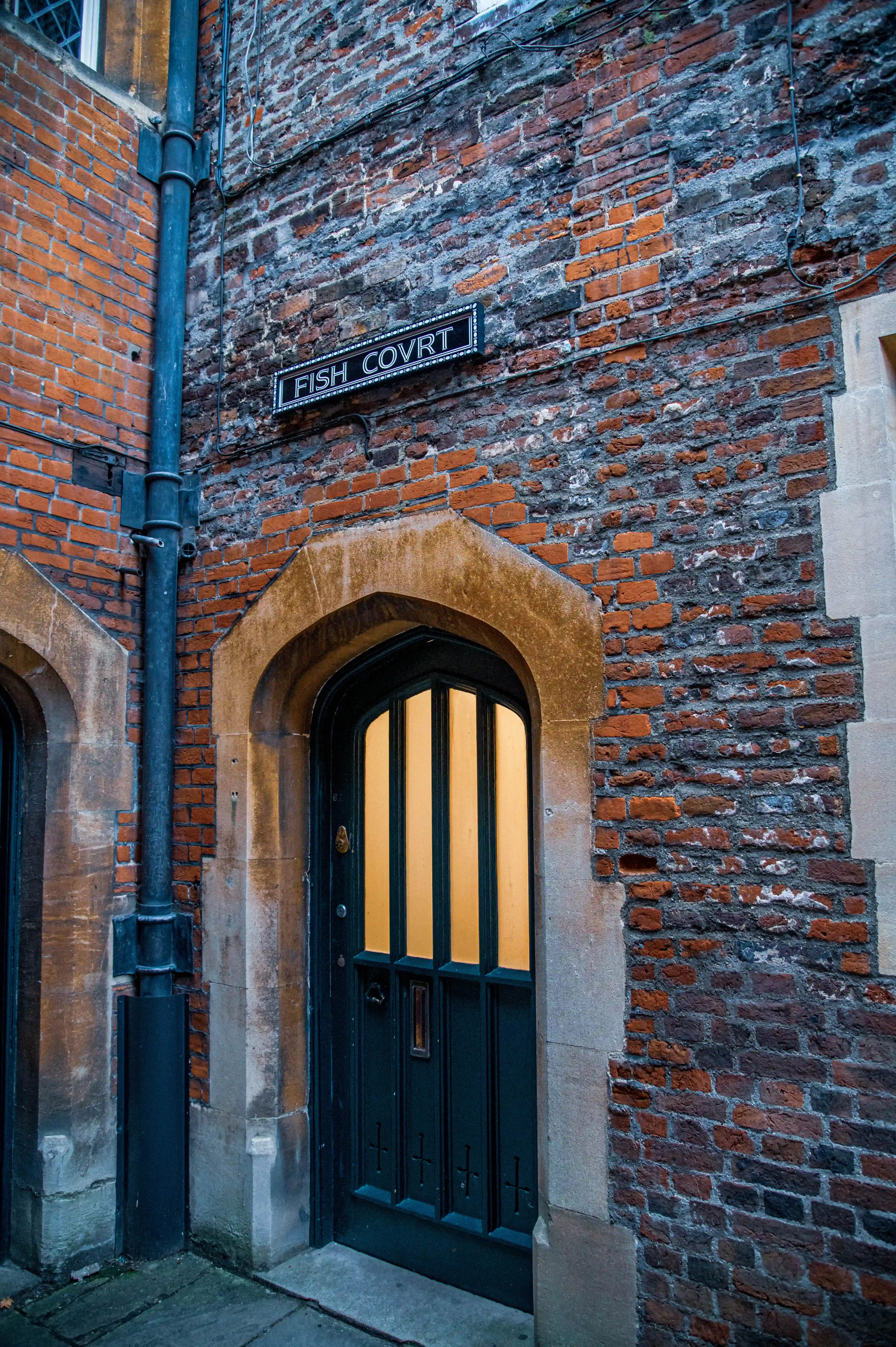 Historic brick archway with “FISH COVRT” sign, dark wooden door and warm interior light.
