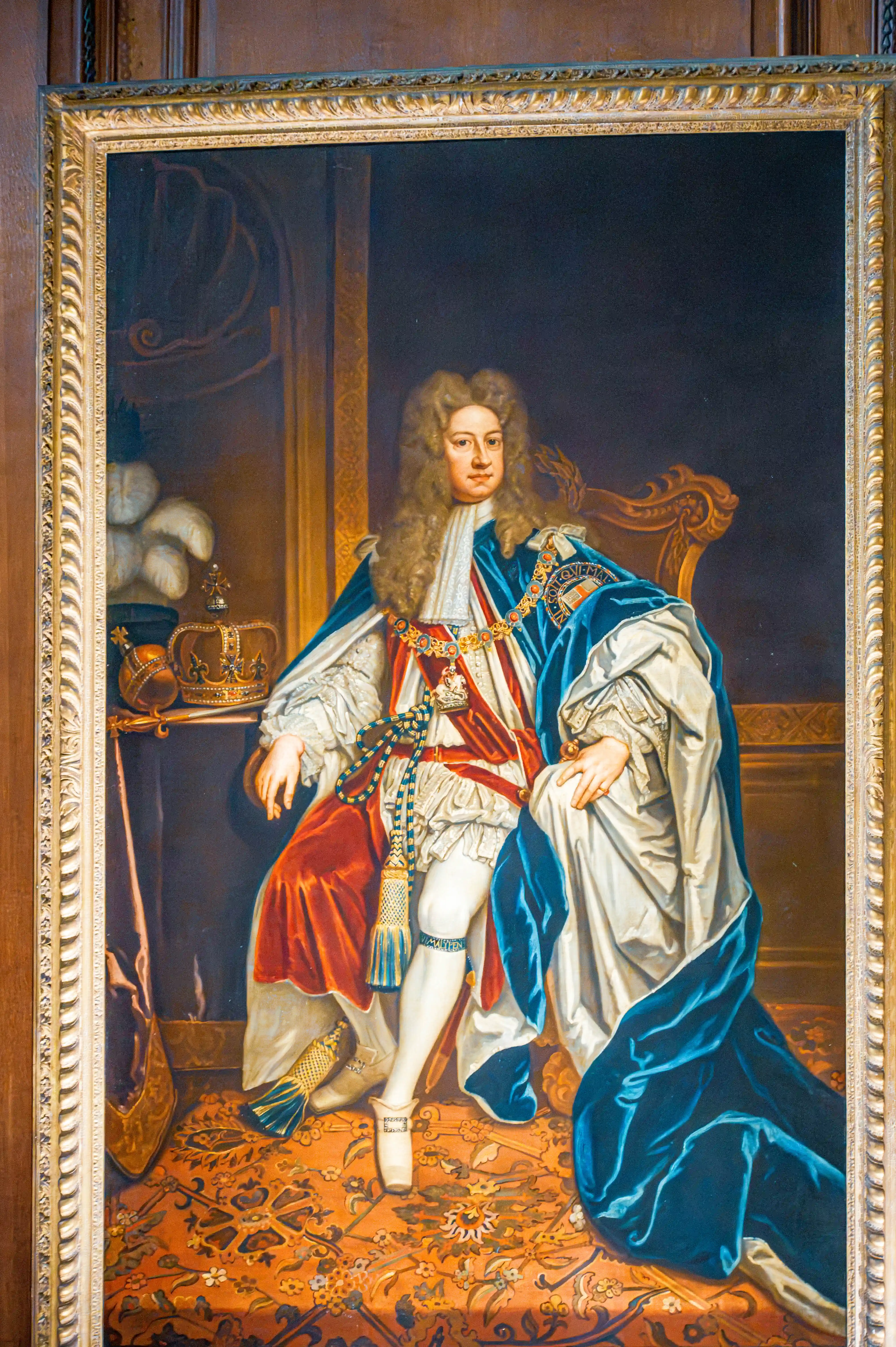 Formal aristocratic portrait featuring ceremonial attire, crown display and ornate gold framing