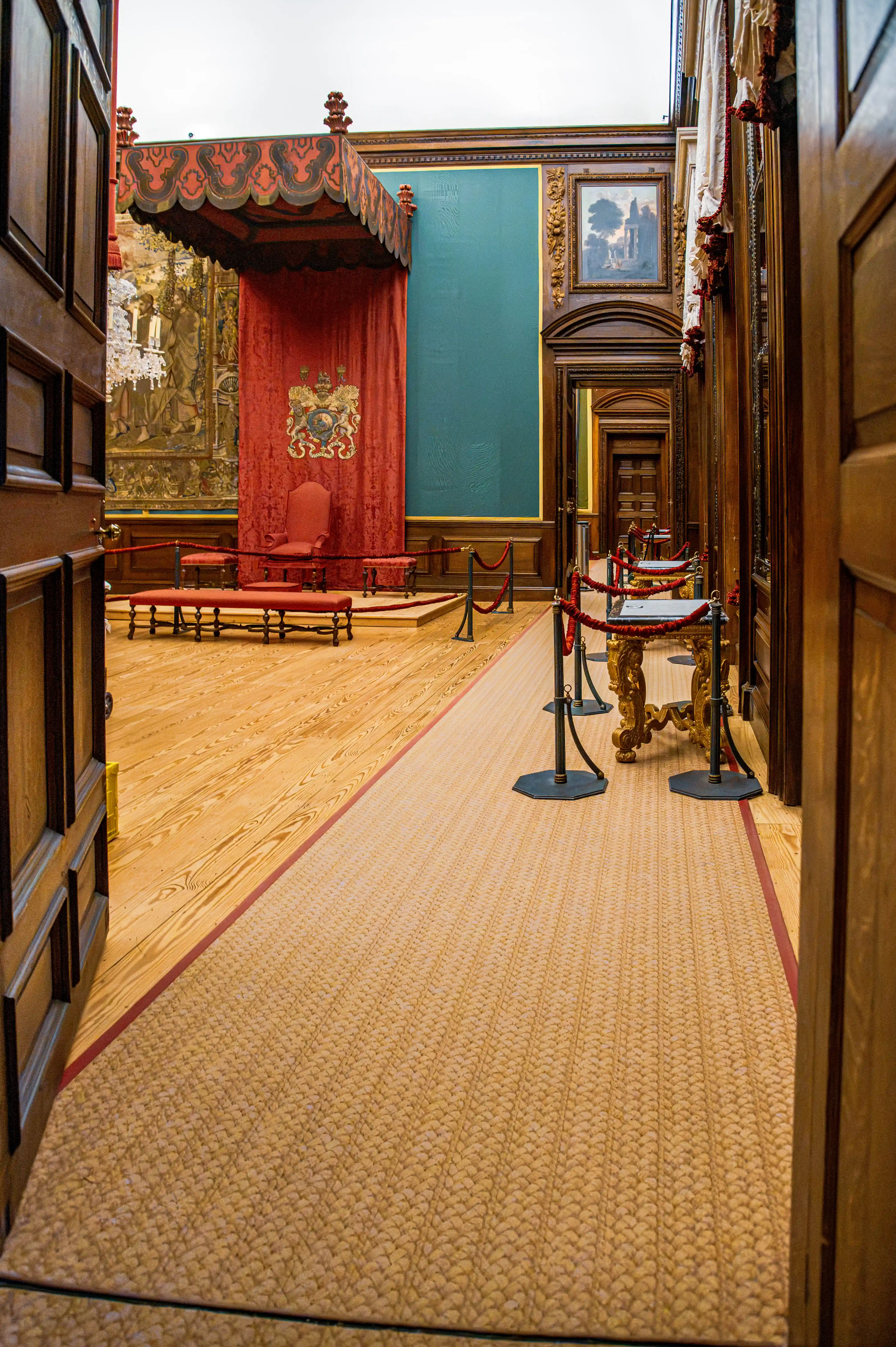 Ceremonial room with red canopy, throne chair, blue panelling and carved interior details viewed through an open doorway.