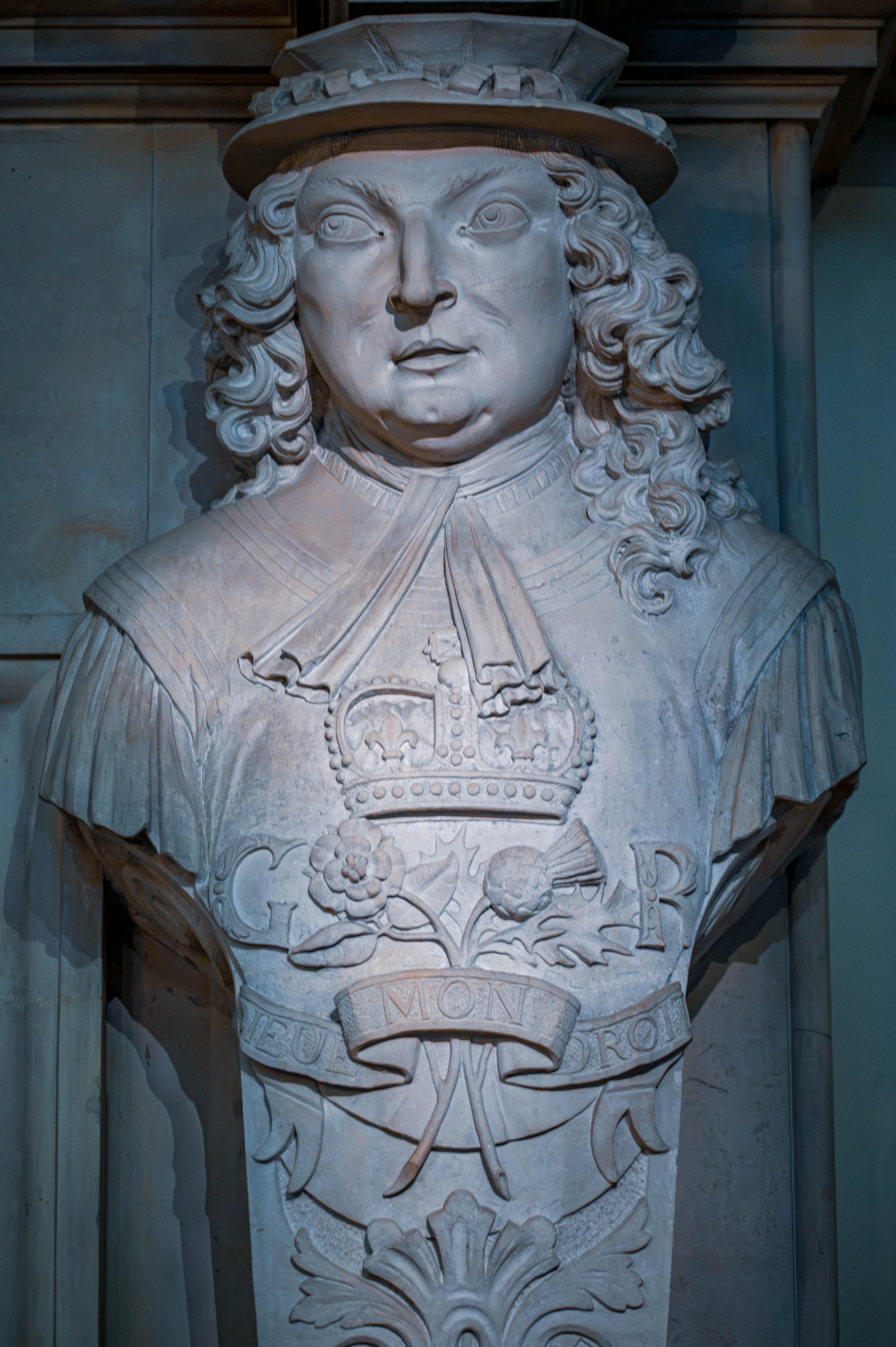 Stone bust with crowned “G R” emblem and motto MON ROY, wearing elaborate period clothing and hat.