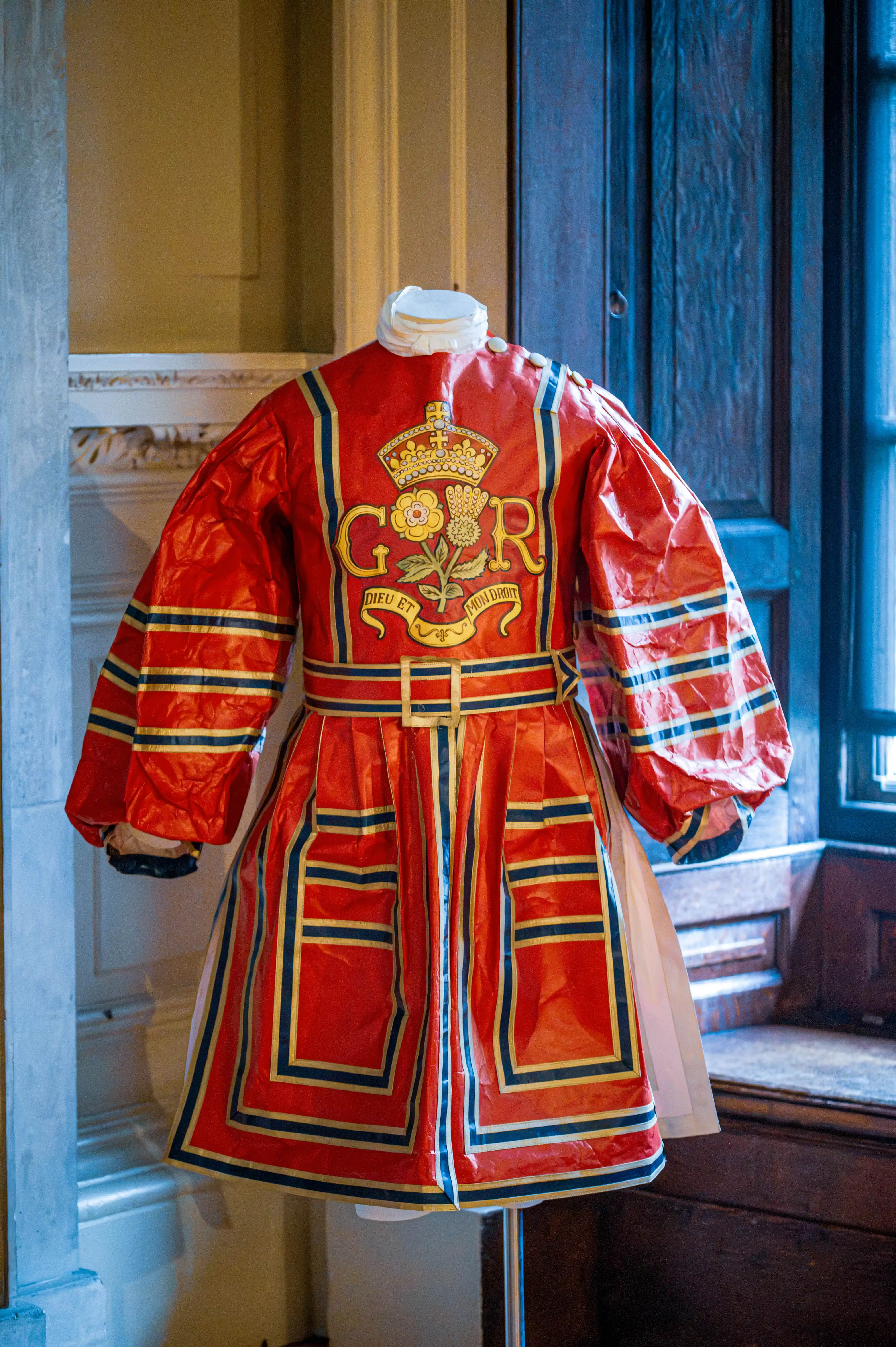 Red ceremonial coat with gold embroidery, crowned “G R” emblem and floral motifs displayed on a mannequin.