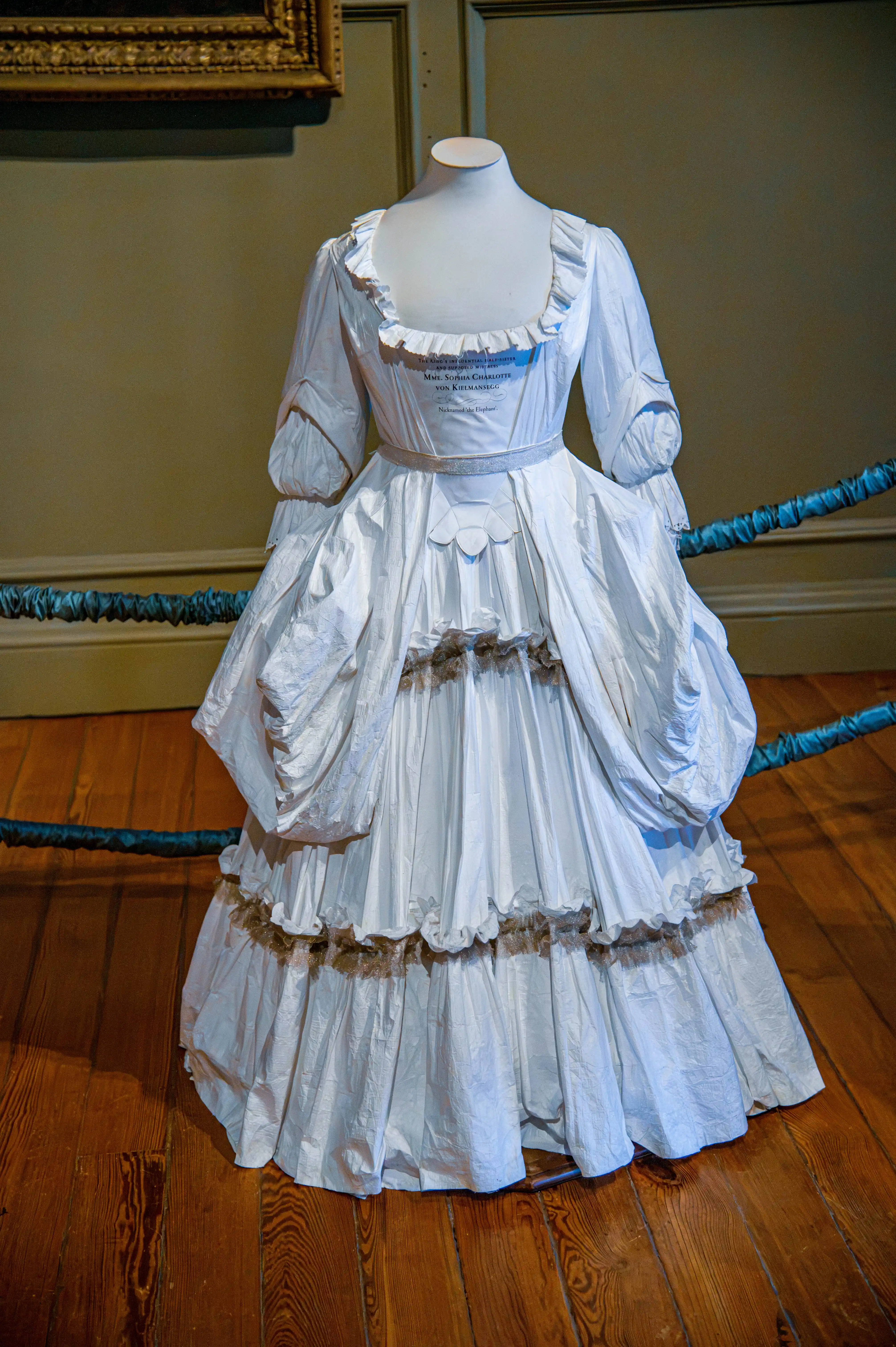 White historic gown with ruffled neckline, gathered sleeves and full draped skirt displayed on a mannequin.