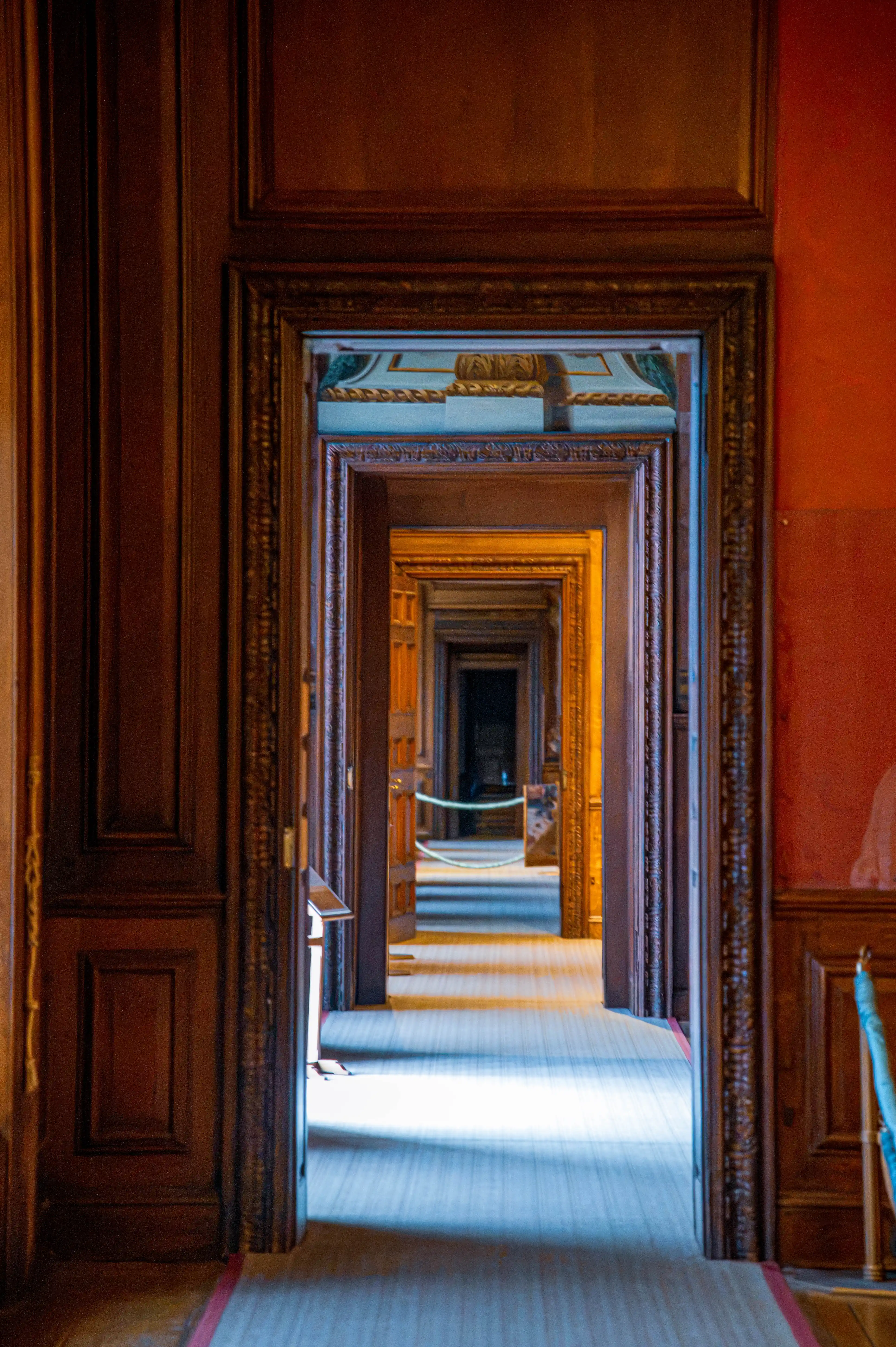 Aligned doorways in a timber-panelled interior forming a long enfilade perspective with carpeted floors.