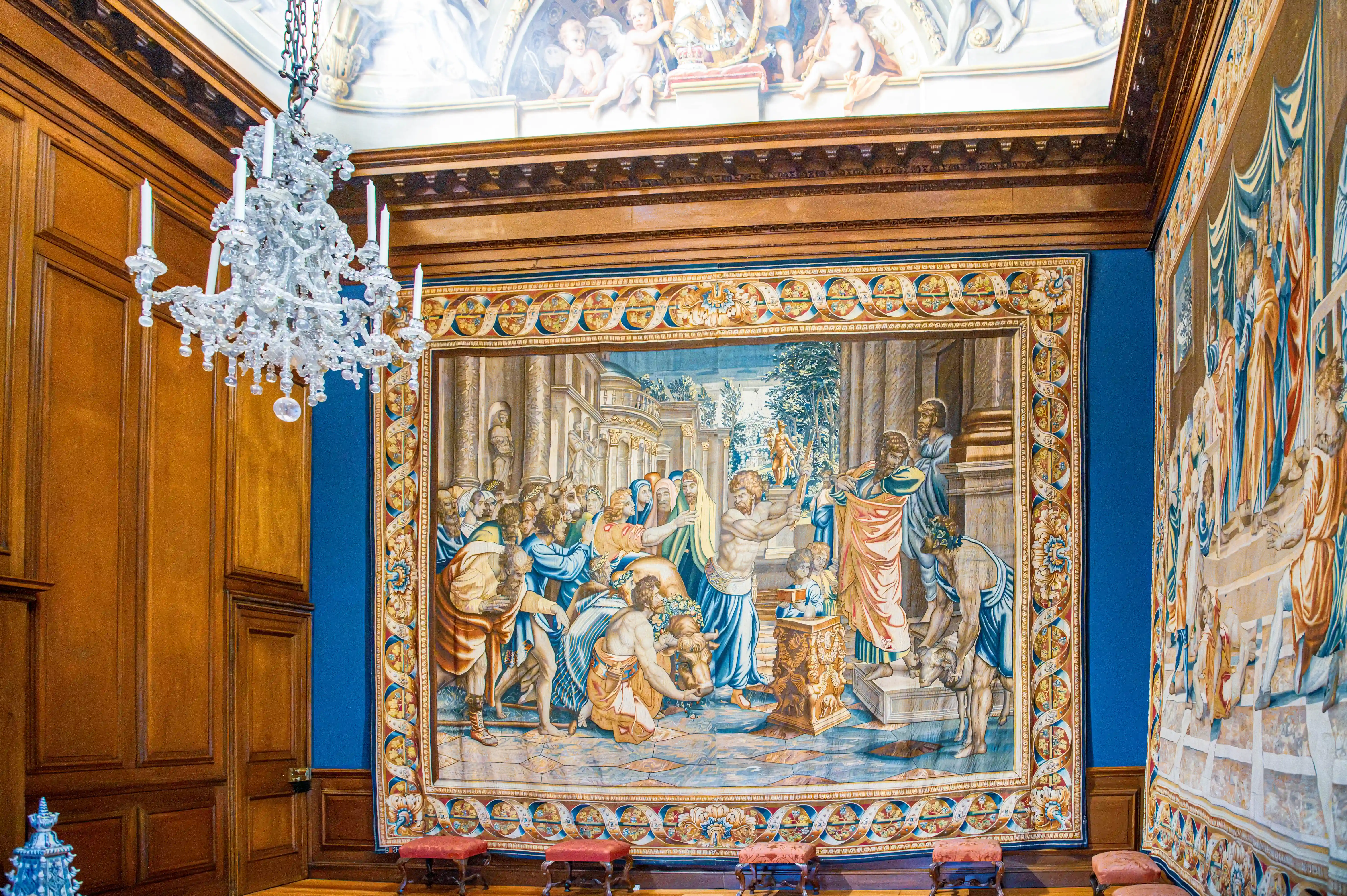Historic room with large narrative tapestries, timber panelling, crystal chandelier and classical painted ceiling.