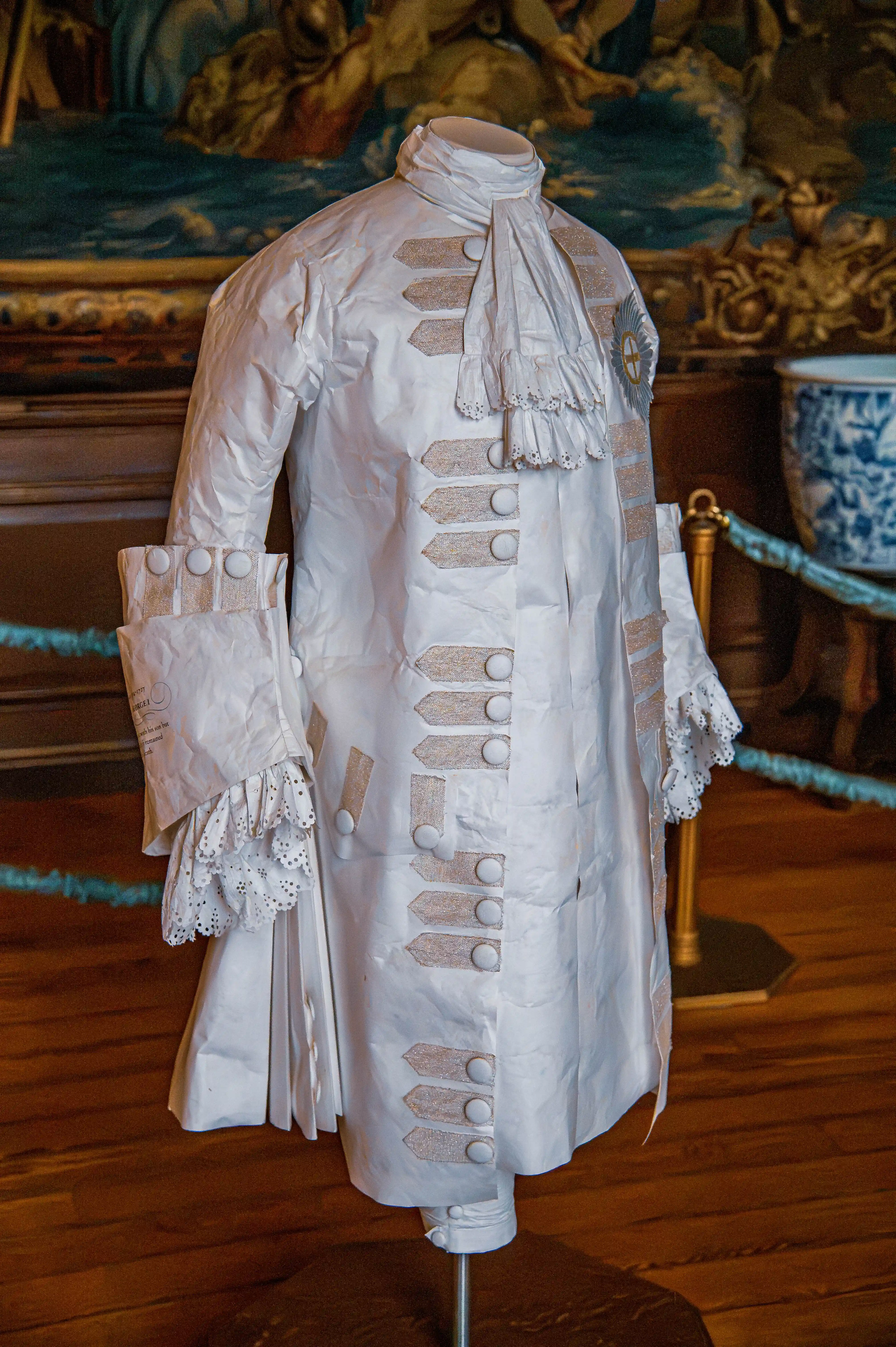 Paper sculpture of an 18th-century men’s coat with lace-trim cuffs and cravat displayed on a mannequin.