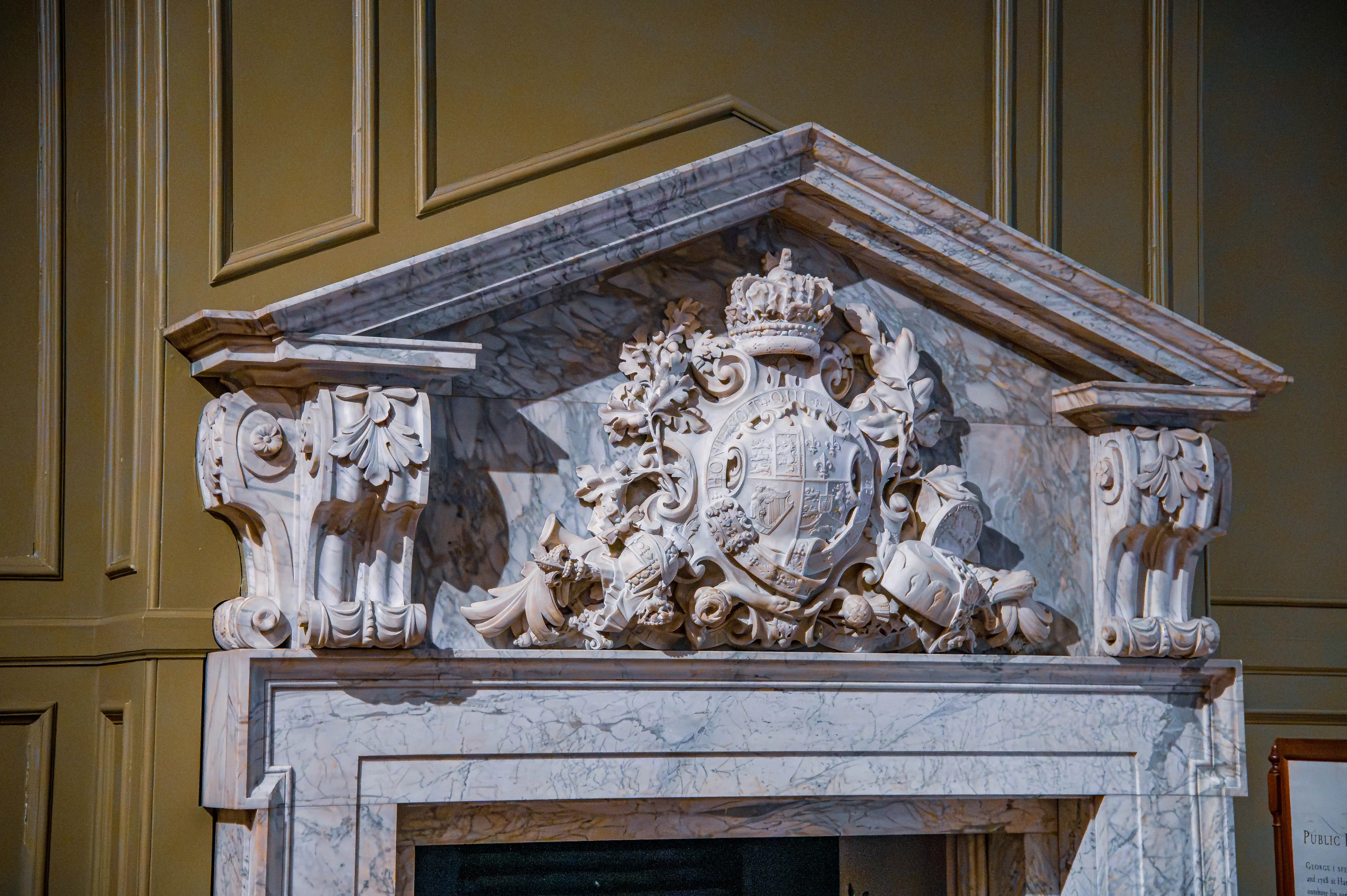 Marble over-door with sculpted heraldic coat of arms, carved brackets and triangular pediment against green panelled wall.