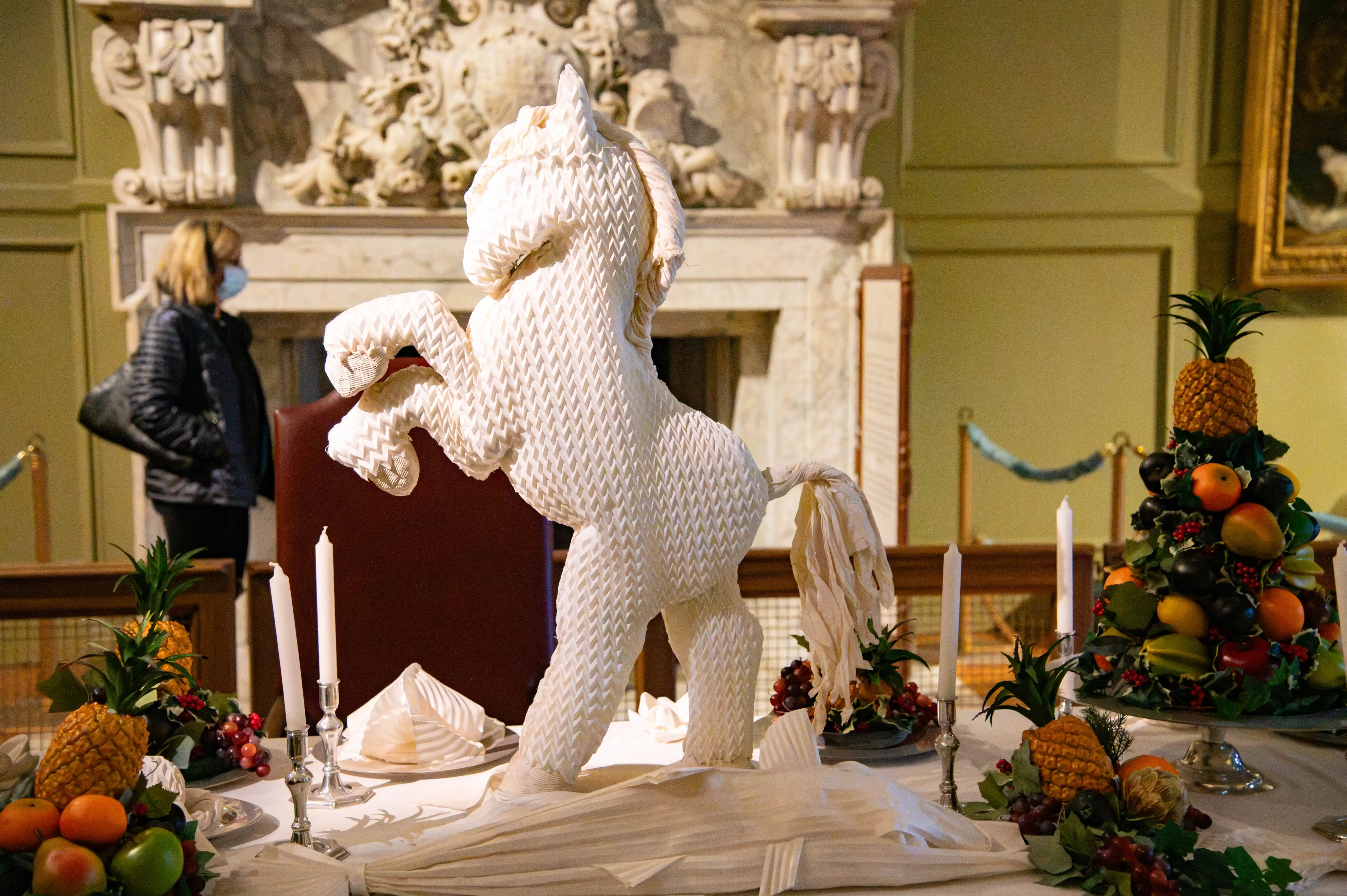 Formal banquet table with a folded napkin horse sculpture, candles and decorative fruit arrangements.