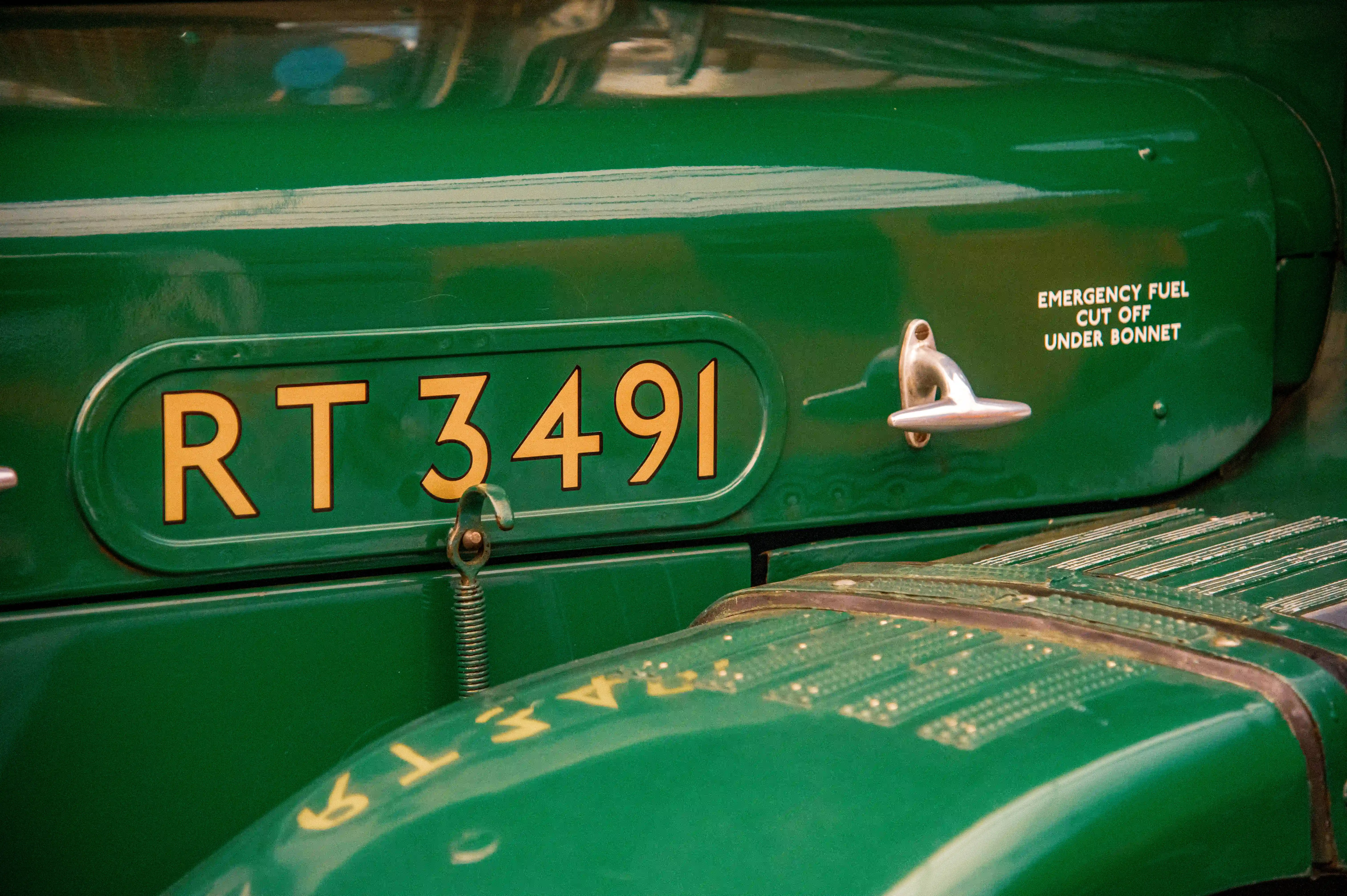 Close-up of a vintage green vehicle's bodywork, featuring an oval registration plate with gold lettering reading 