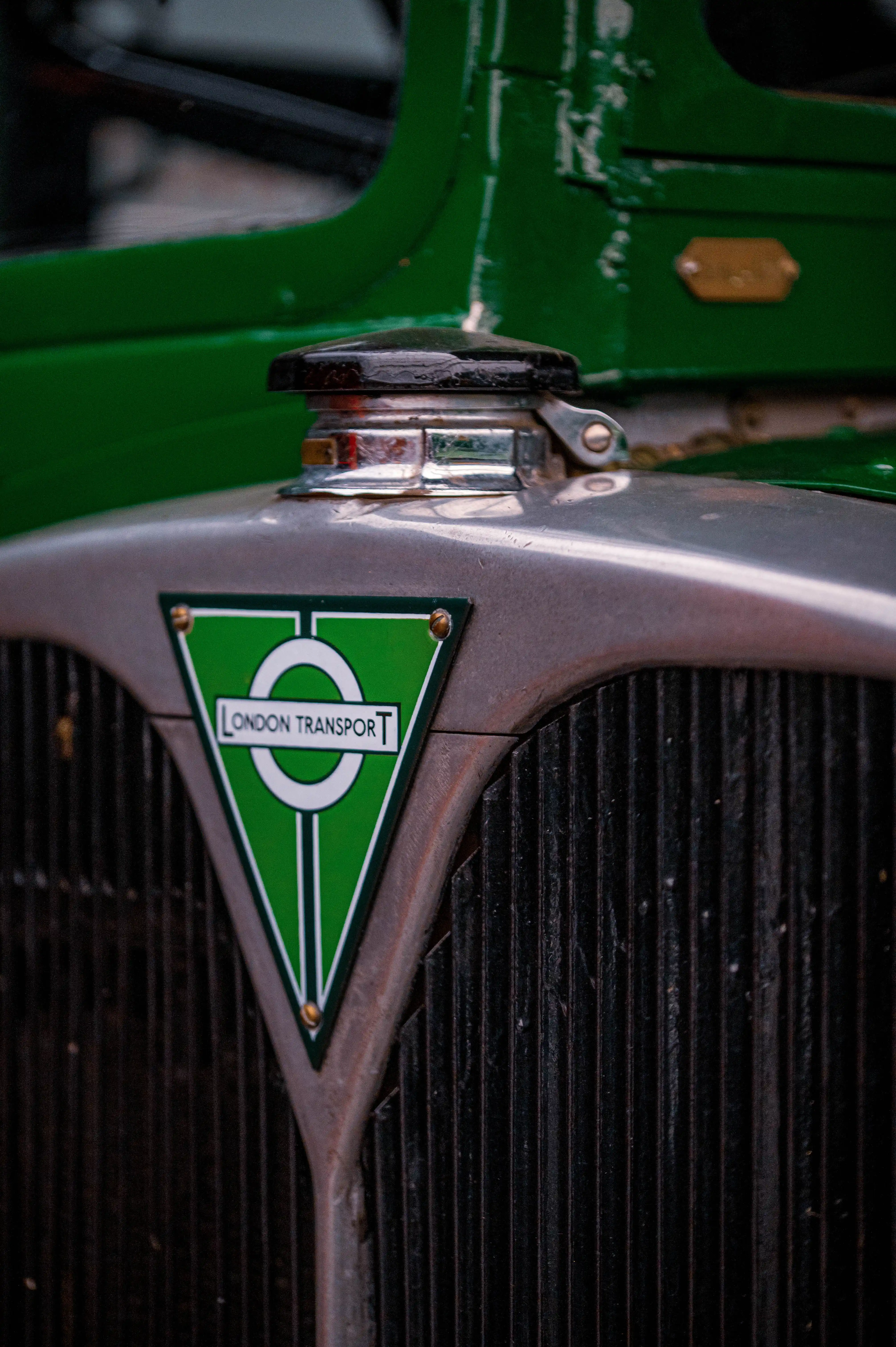 Close-up of the front of an old green and grey vehicle, focusing on the radiator grille and a triangular green emblem that reads 
