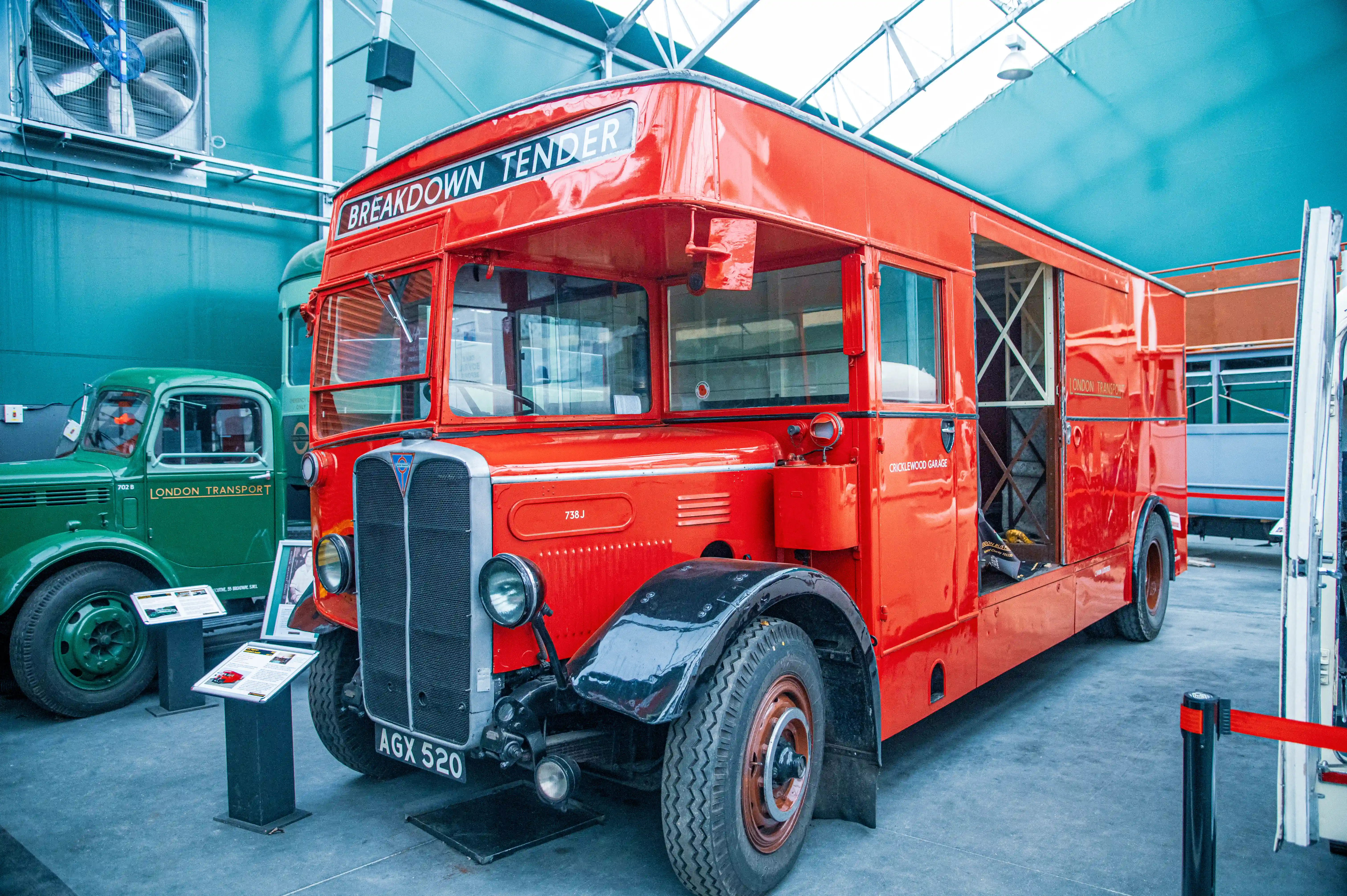 A bright red vintage London Transport breakdown tender bus with the text BREAKDOWN TENDER on top and AGX 520 on its license plate. A green London Transport truck is partially visible to the left.