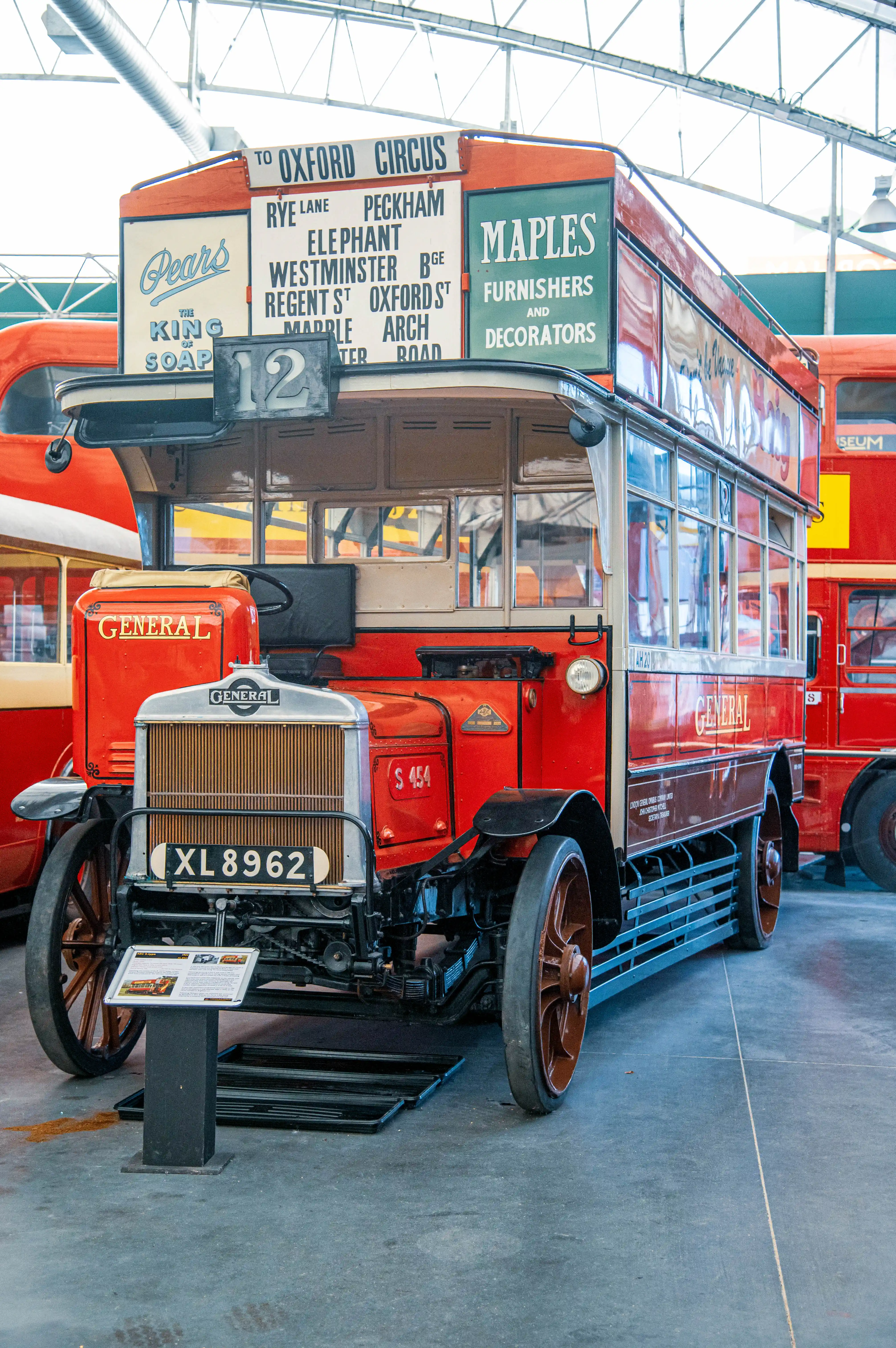 Front view of a vintage red London double-decker bus with route information to Oxford Circus and advertisements for Pears soap and Maples.