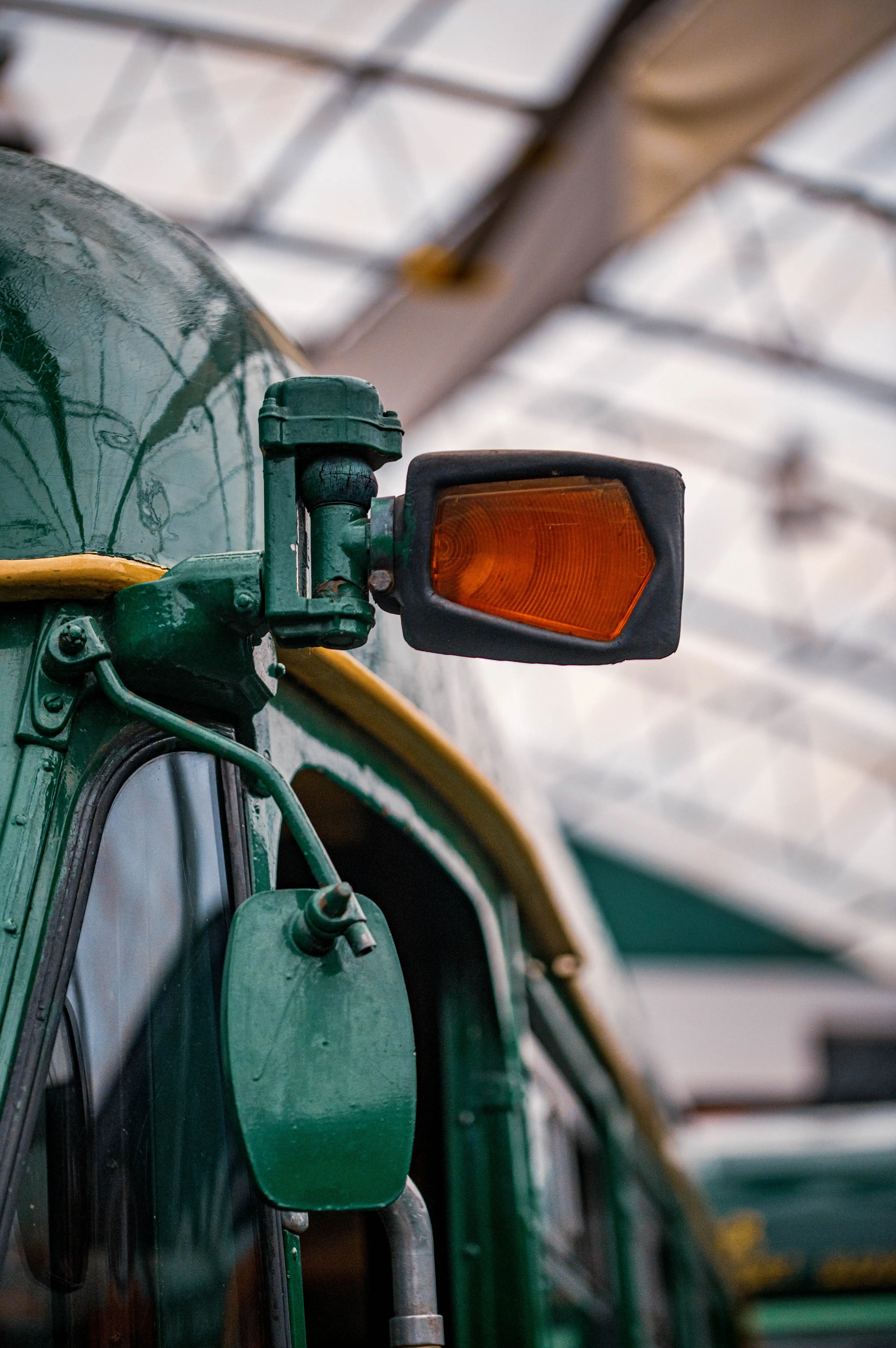 Close-up of an old green Bus's exterior, focusing on a rectangular amber indicator light and a wing mirror.