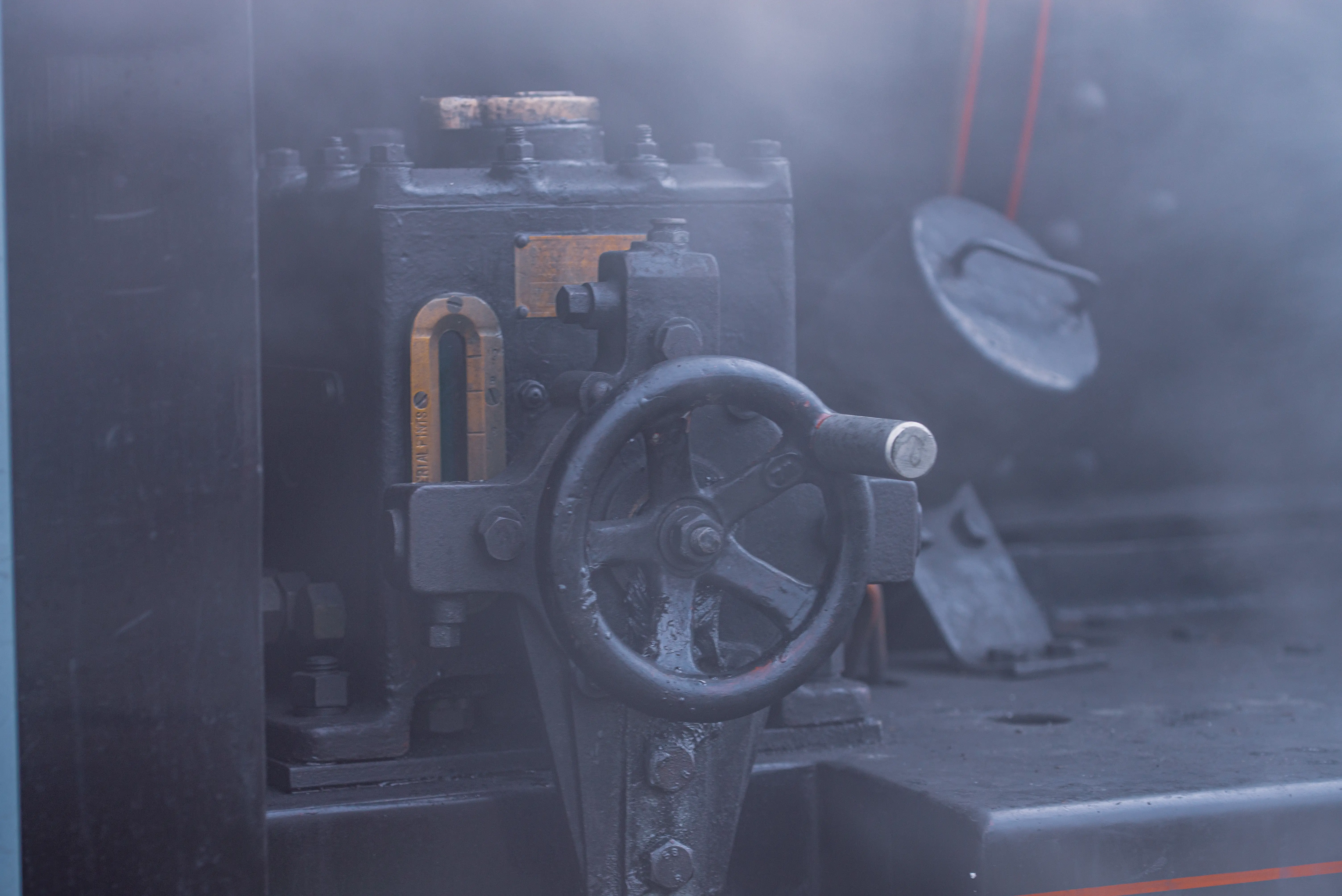 Close-up of a metal handwheel and valve assembly with a brass gauge plate, partly obscured by steam.