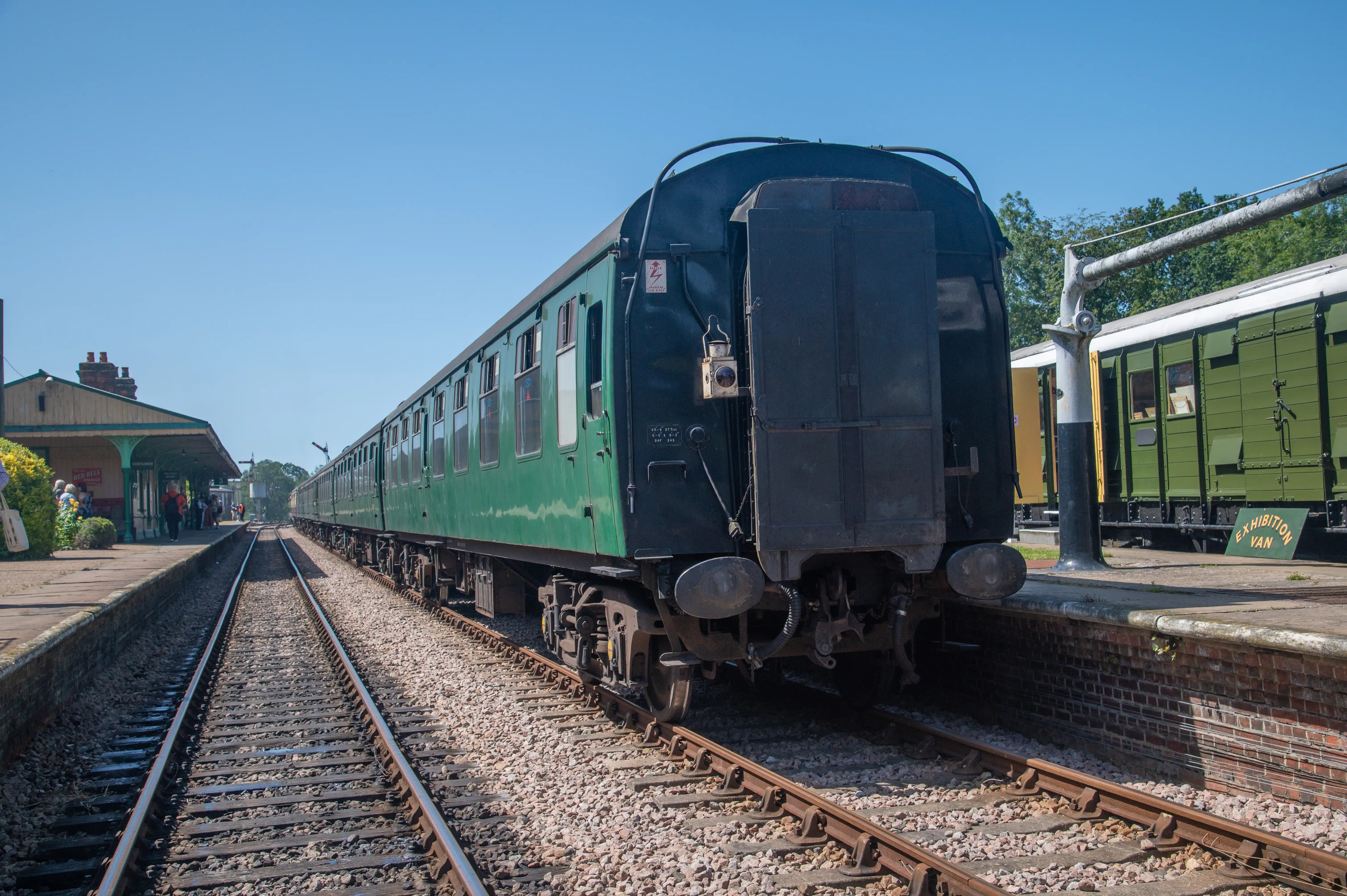 An image showing a pair of old, rusty railway semaphore signals, set against a bright blue sky. One signal arm points upwards and to the right, while the other points horizontally to the left. Both arms are painted with red and white stripes. The supporting structure is made of weathered metal.