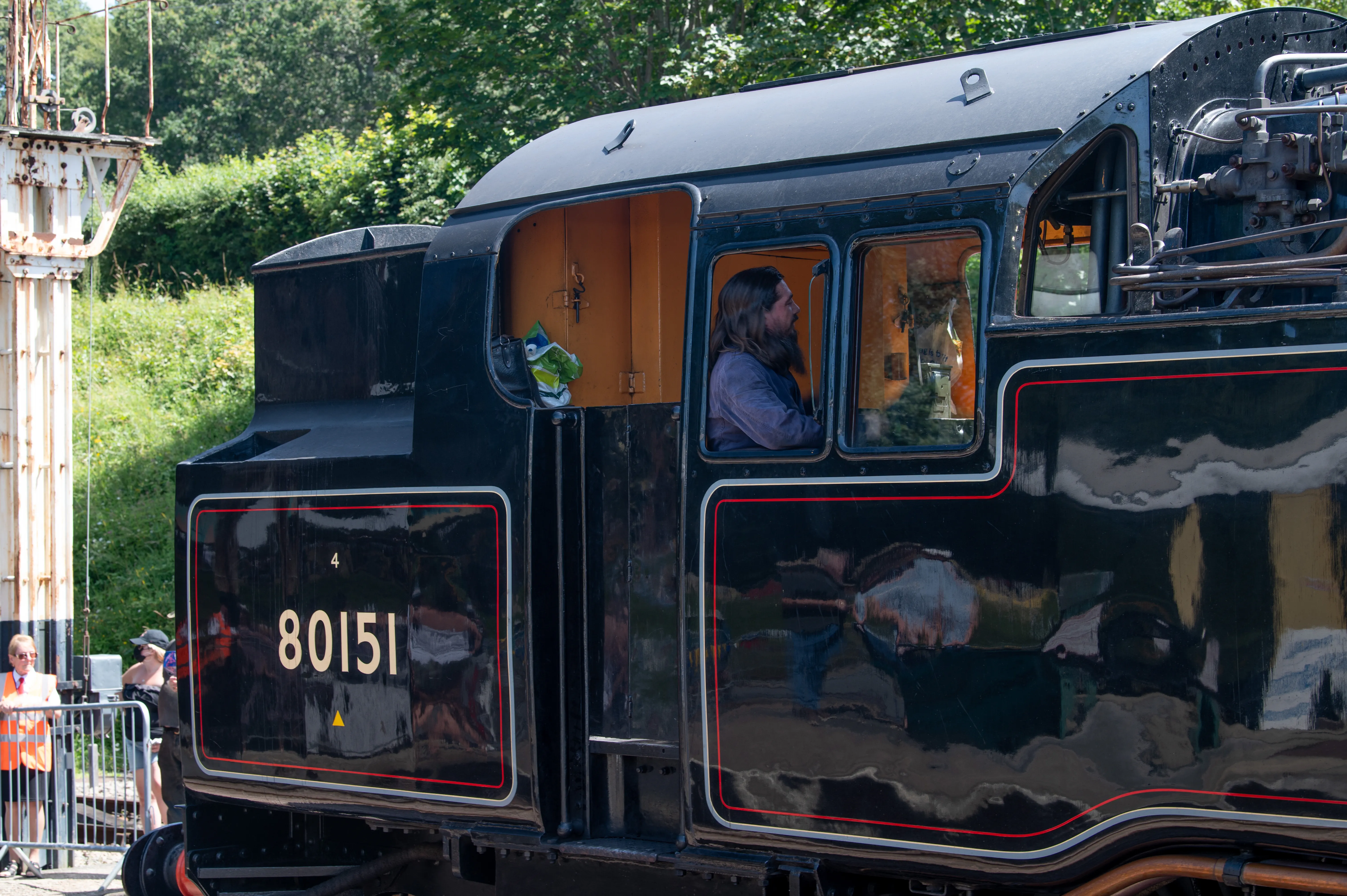 A close-up of the side of a black steam locomotive, showing the driver in the cab and the number 80151 on the side.