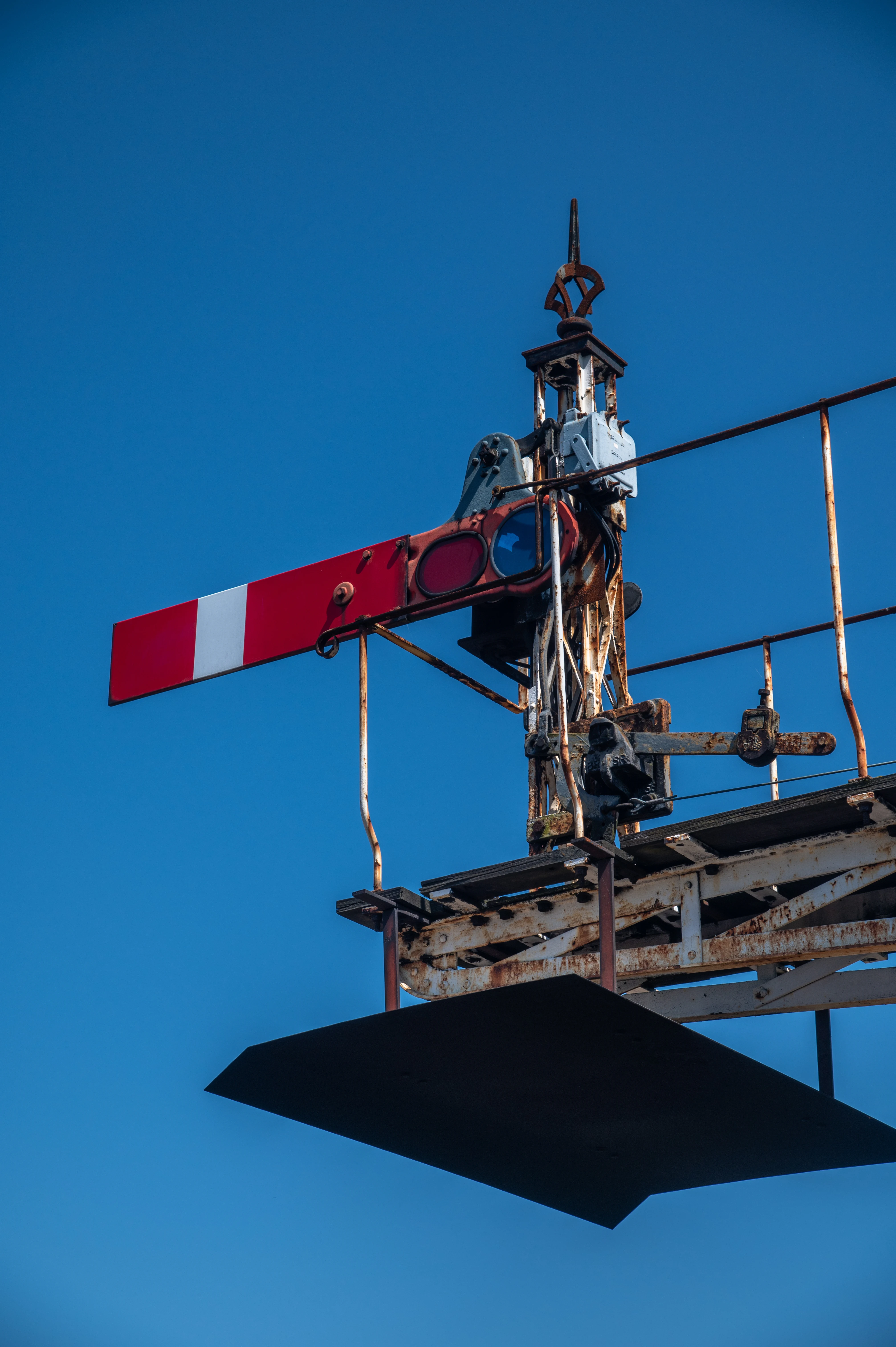 A close-up, low-angle view of a vintage railway semaphore signal. The signal arm is red with a white stripe and extended horizontally, indicating a 