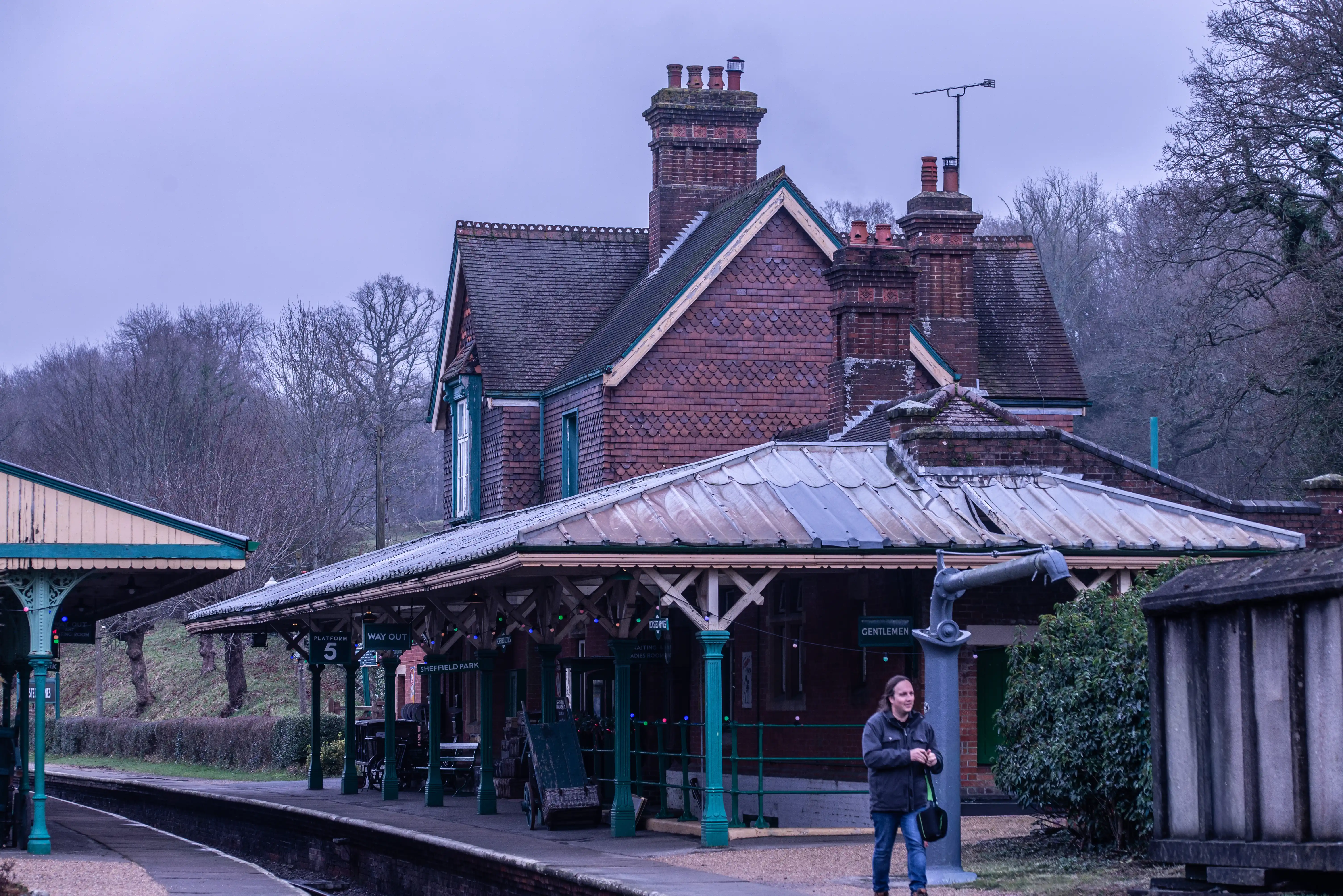 Historic Horsted Keynes railway station with red-brick buildings, green columns and period platform signage.