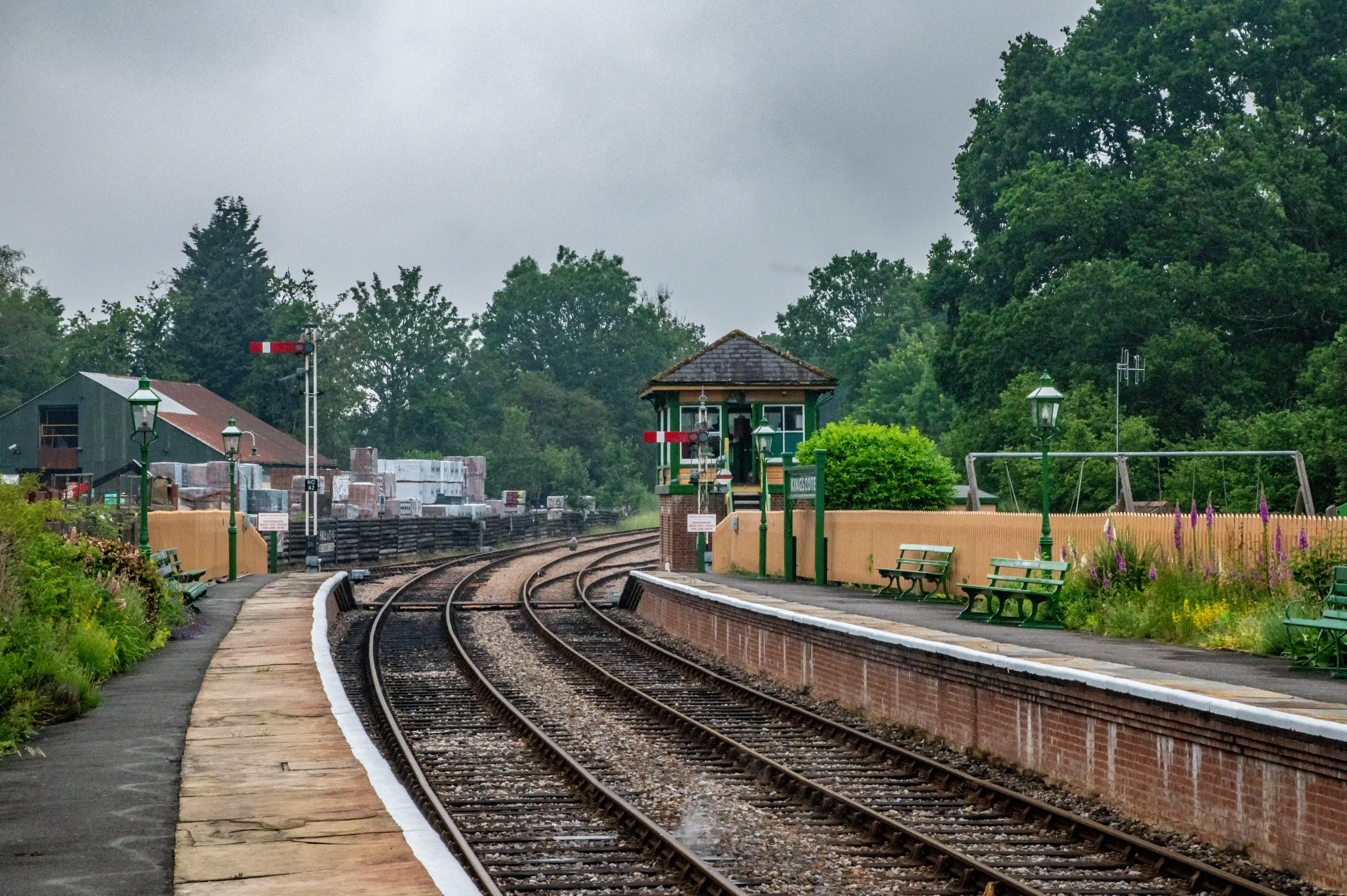 A black steam locomotive is visible on the tracks at a railway station. A vintage signal box with a sign reading HORSTED KEYNES is to the right. Wooden railway wagons are in the foreground.