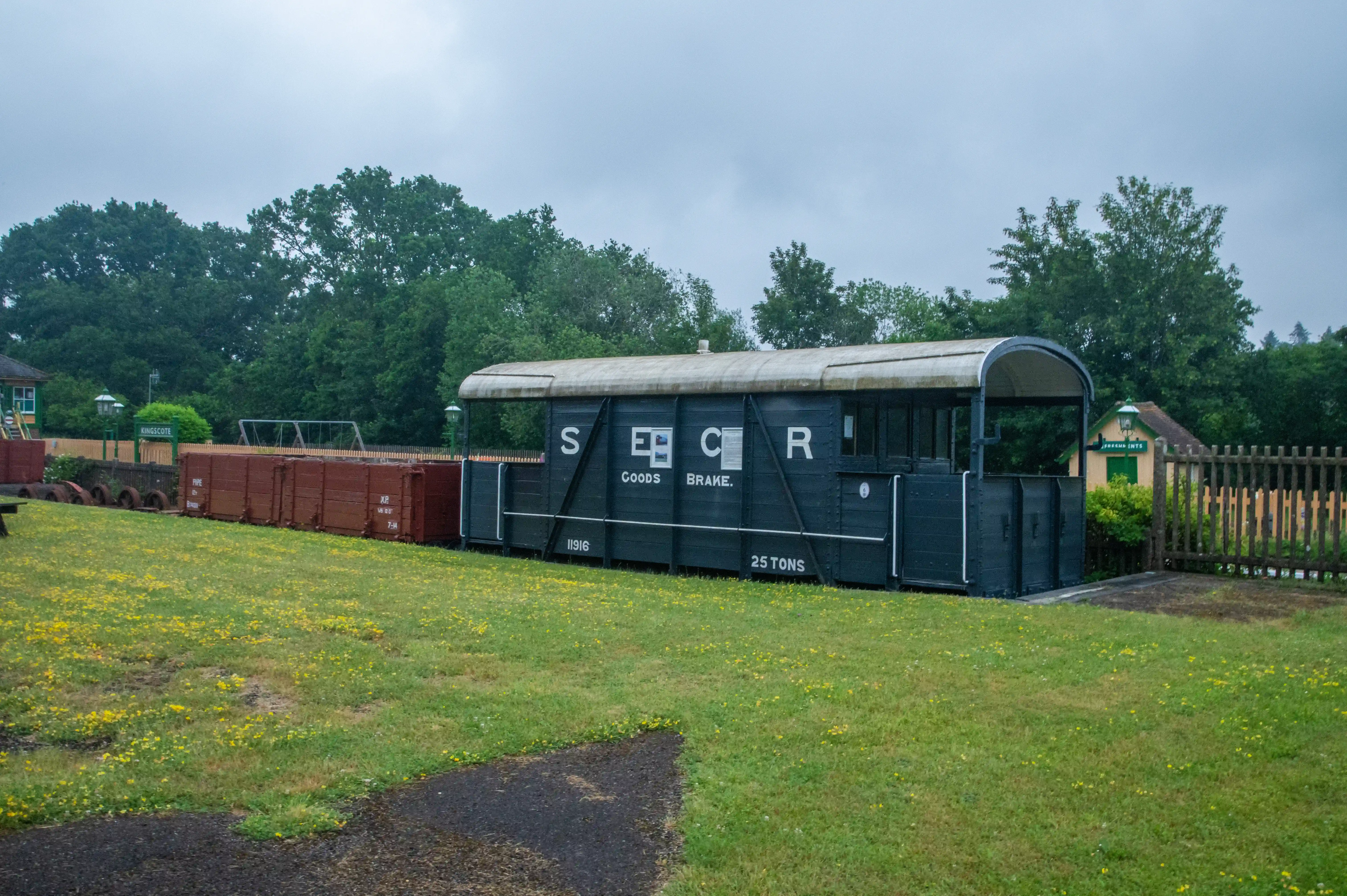 SECR goods brake van in a heritage railway yard at Kingscote, surrounded by vintage freight wagons and trees under an overcast sky.