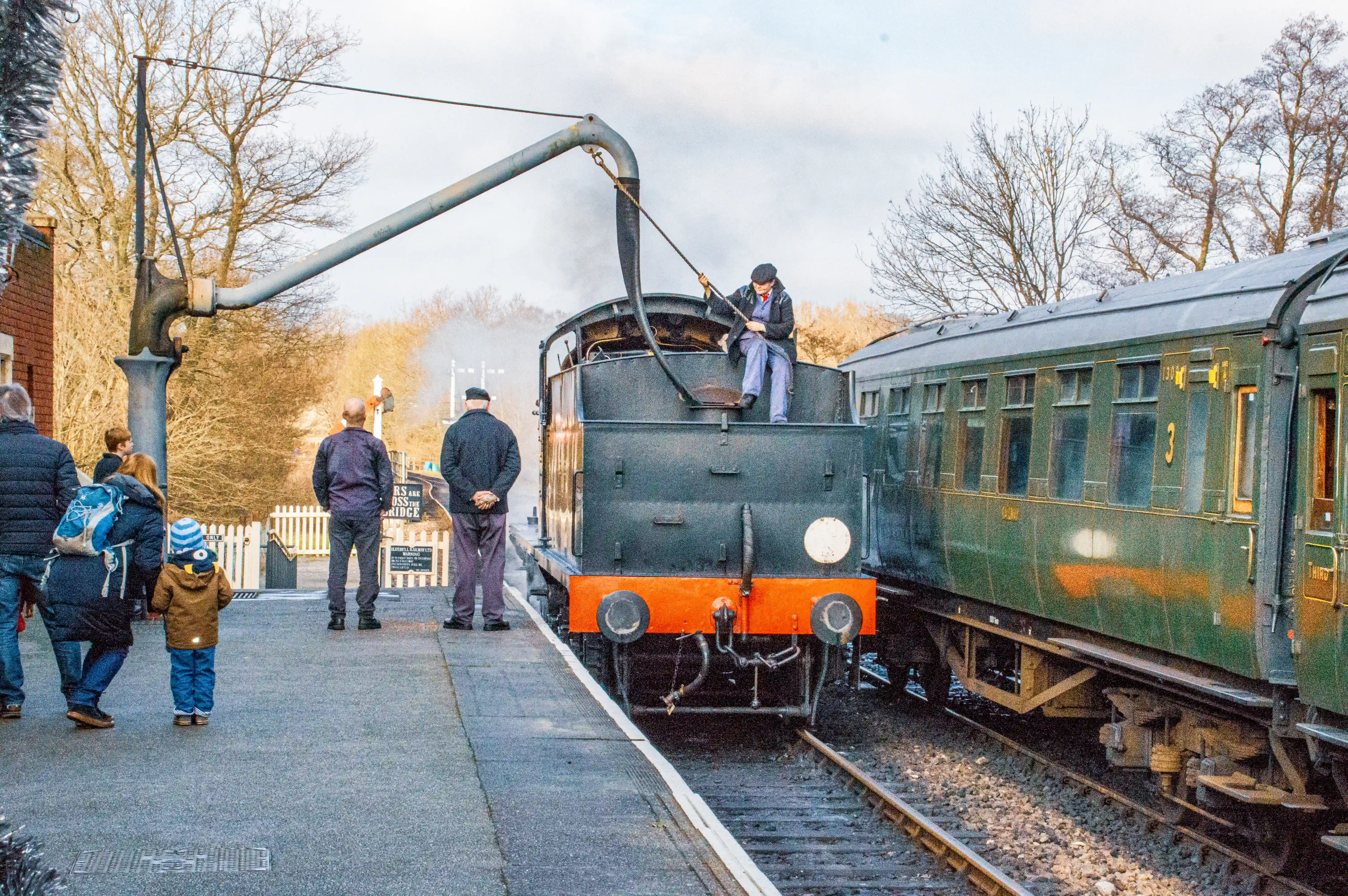 A steam locomotive numbered 30541, with a man in the cab, sits at a train station next to a green carriage, with a coal tender full of fuel.