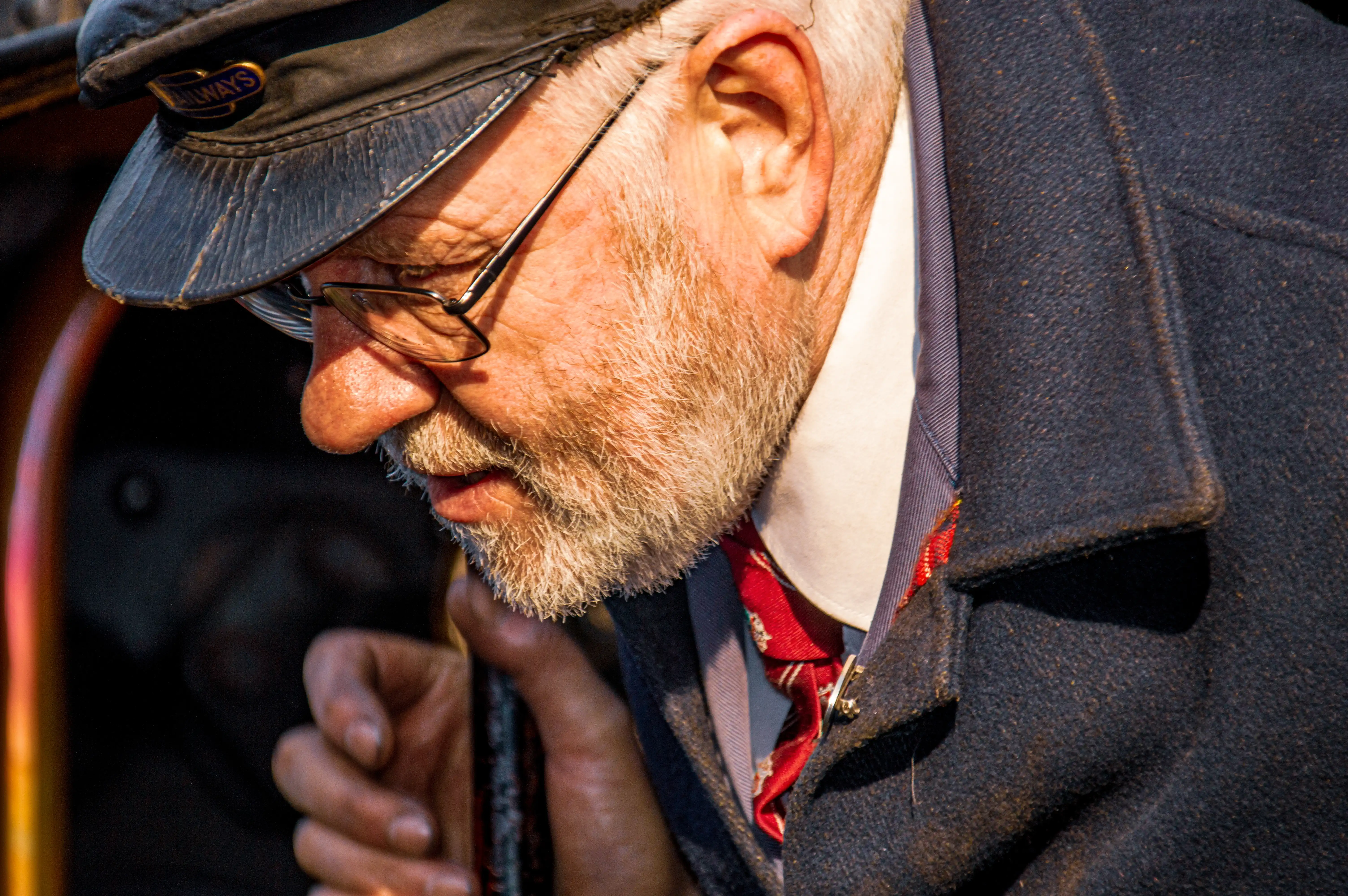 Close-up portrait of an elderly man with a white beard and glasses, wearing a train driver's cap and jacket.