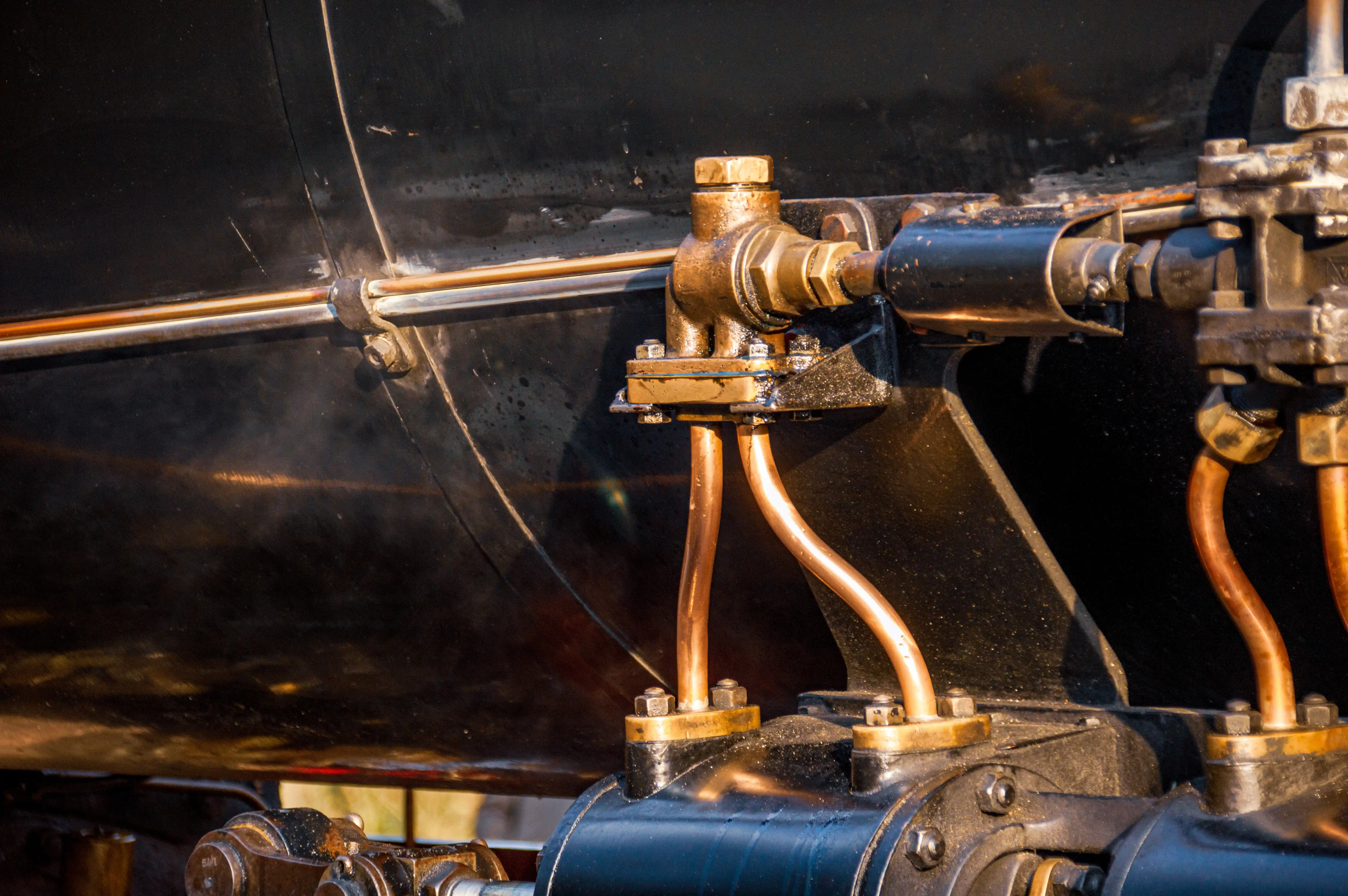 Close-up of brass and copper pipes and a valve assembly attached to a dark, textured surface, suggesting a steam engine.