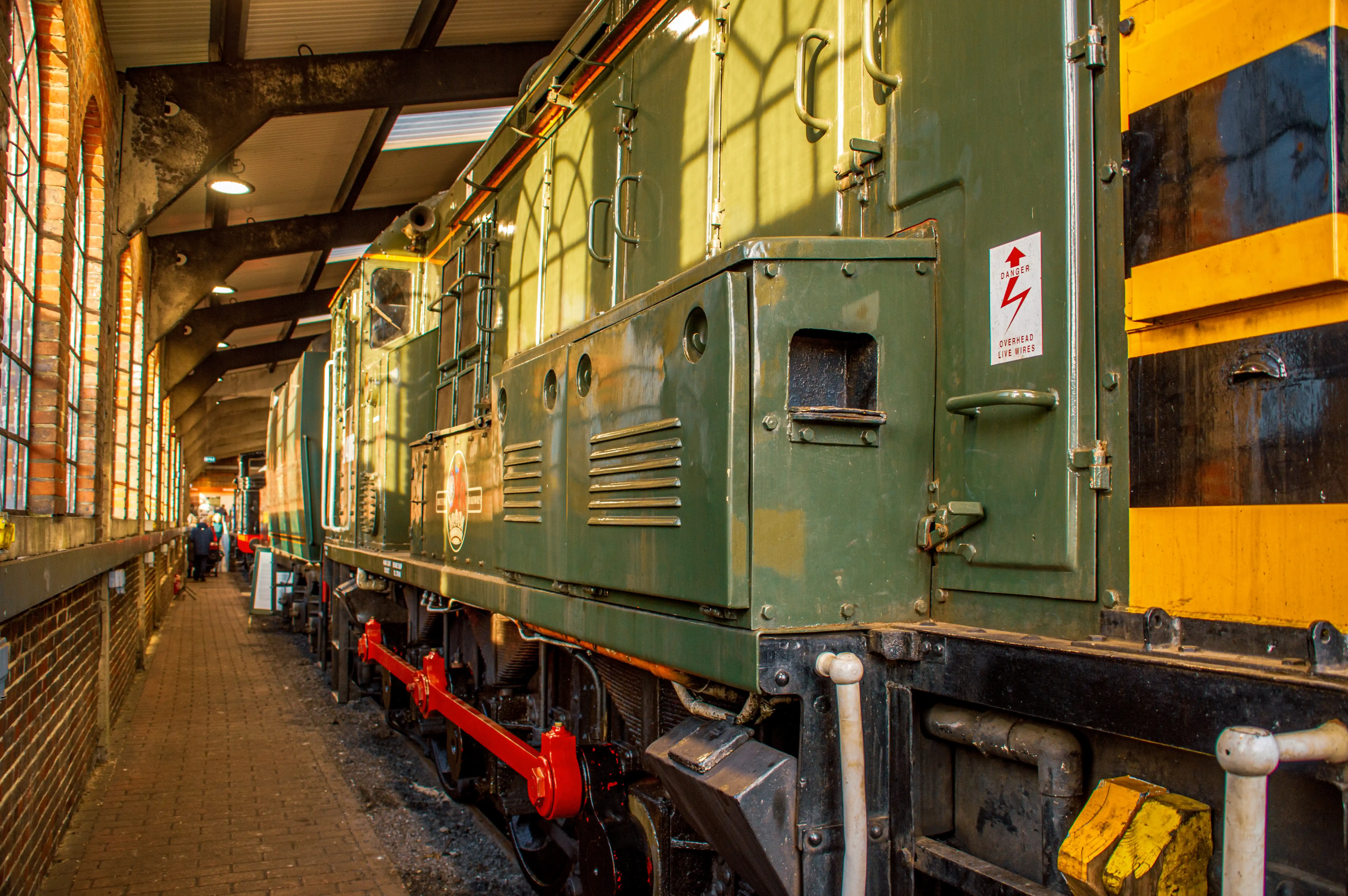 Green and yellow diesel locomotive inside a brick-walled railway shed with visible wheels, rods and a red connecting rod.