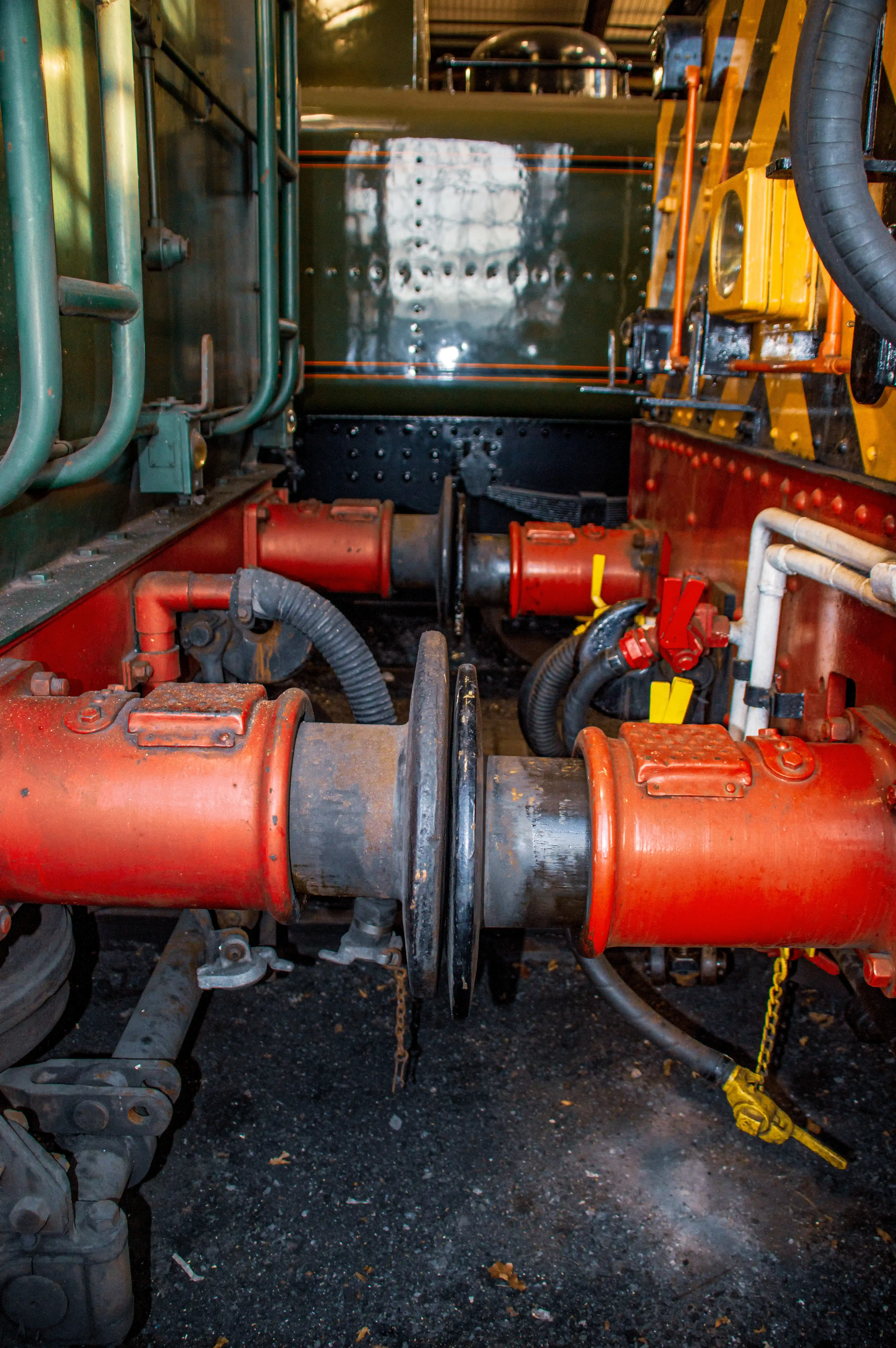 Close-up view of the red-painted buffer beams and coupling mechanism between two old steam trains. The buffing gear is designed to absorb impact between carriages.