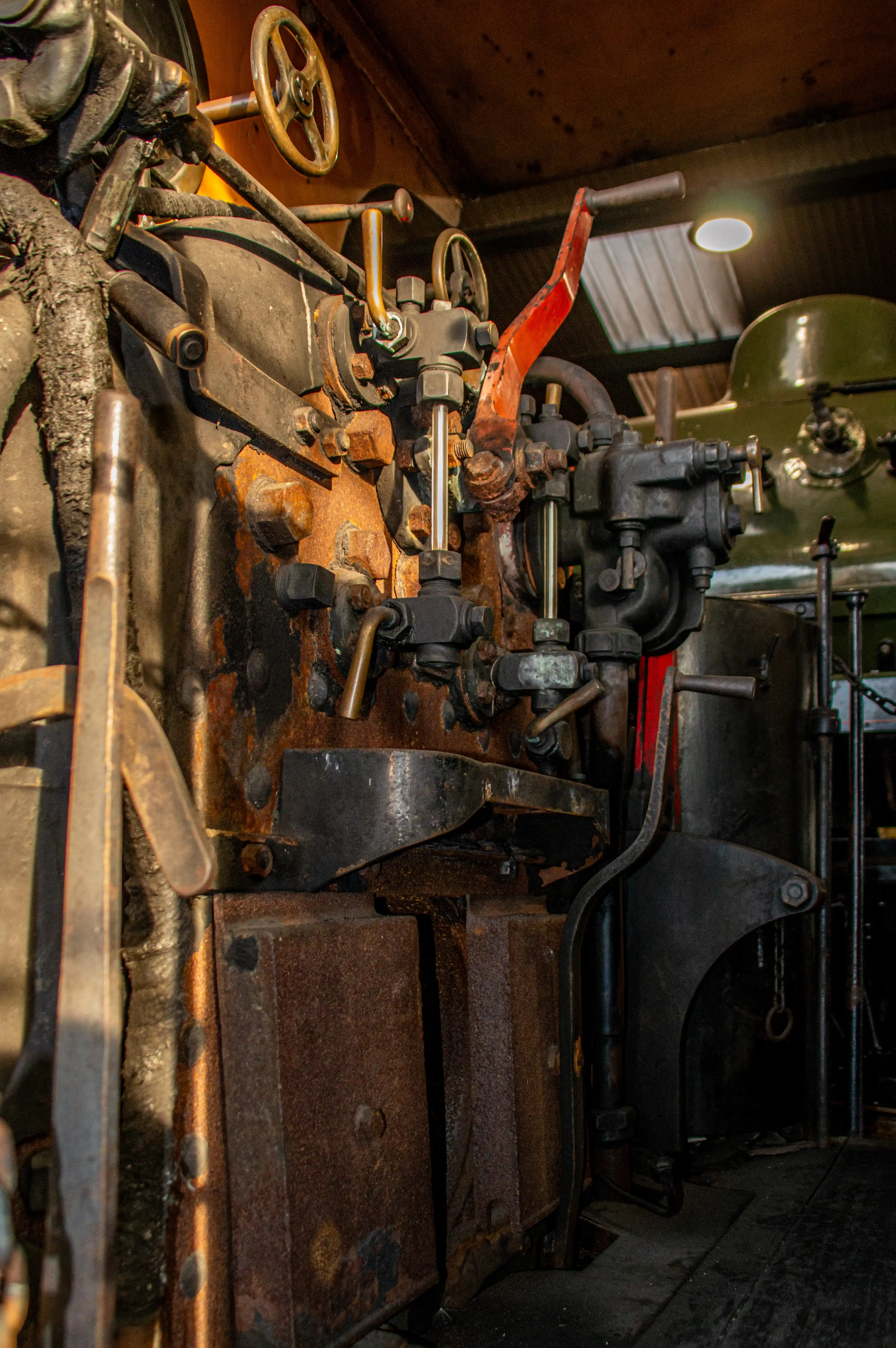 Close-up of old steam engine controls, showing levers, wheels, pipes, and a rusted metal boiler.
