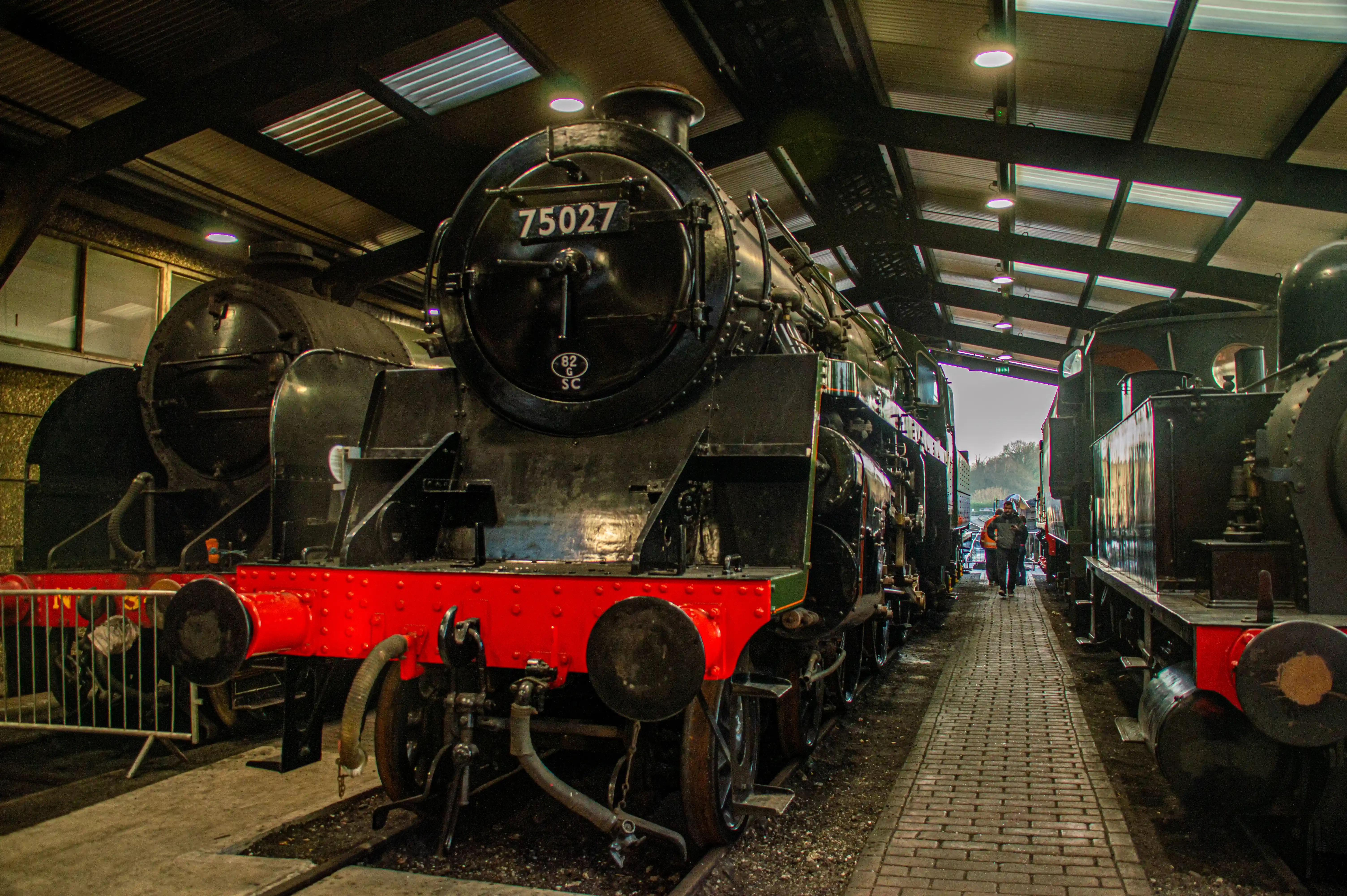 Steam locomotive cab interior showing pressure gauges, brass pipes, valves and a red regulator lever.
