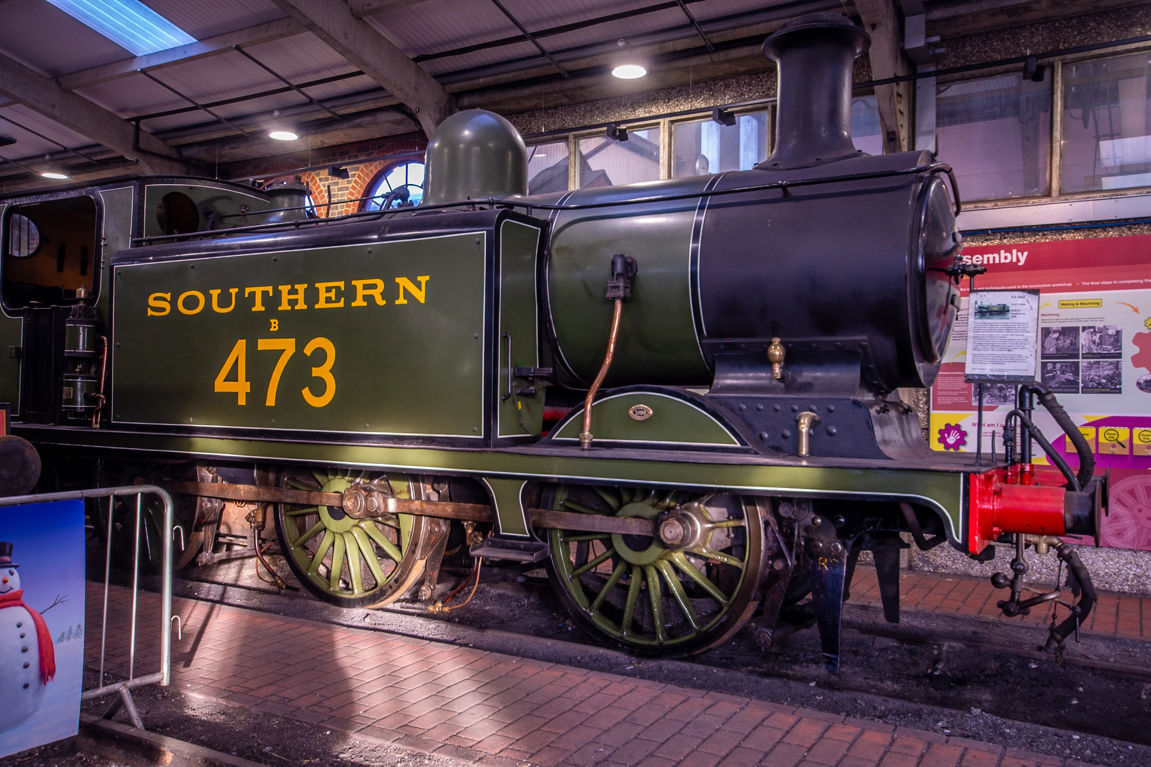 Steam locomotive cab interior showing pressure gauges, brass pipes, valves and a red regulator lever.