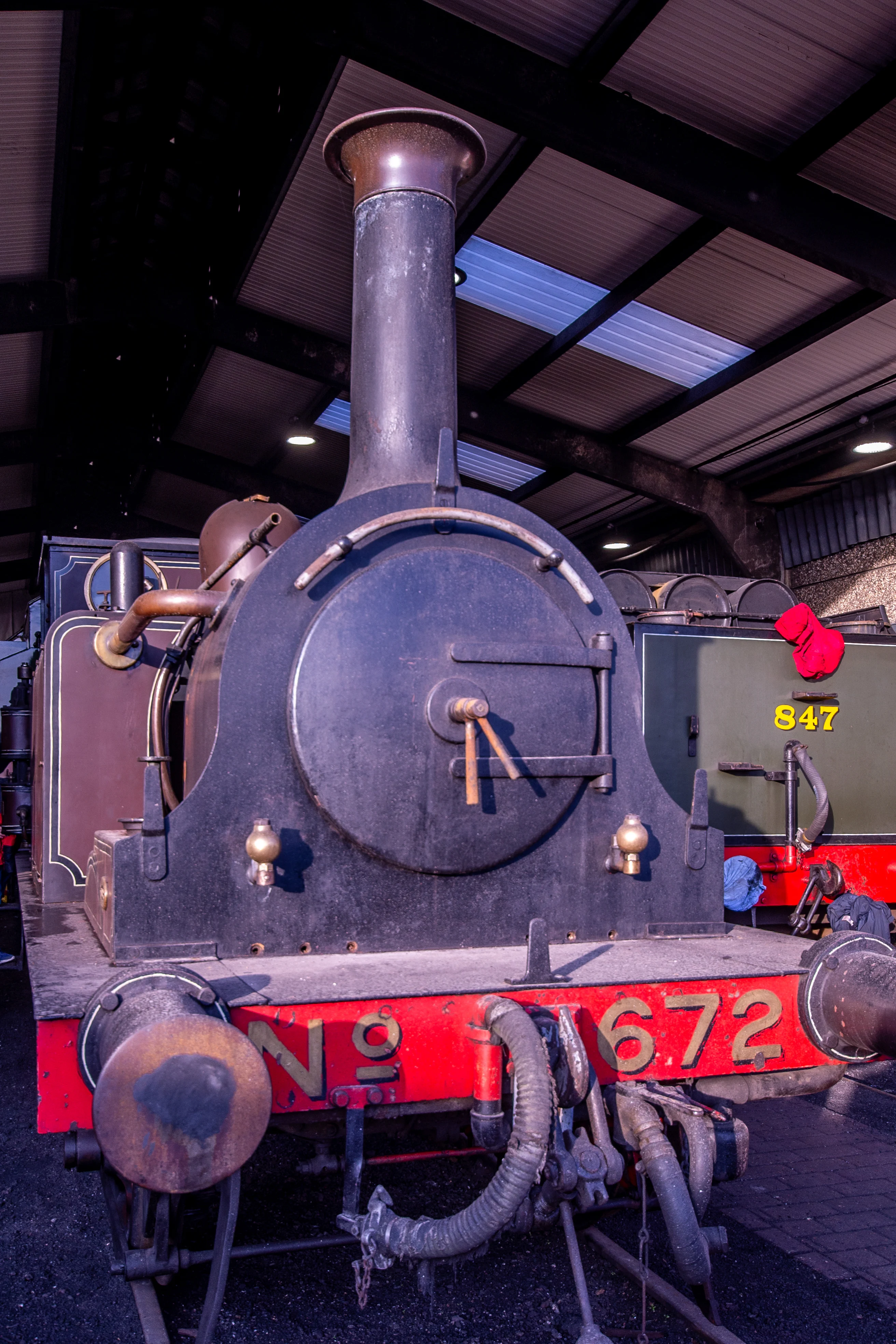 Steam locomotive cab interior showing pressure gauges, brass pipes, valves and a red regulator lever.