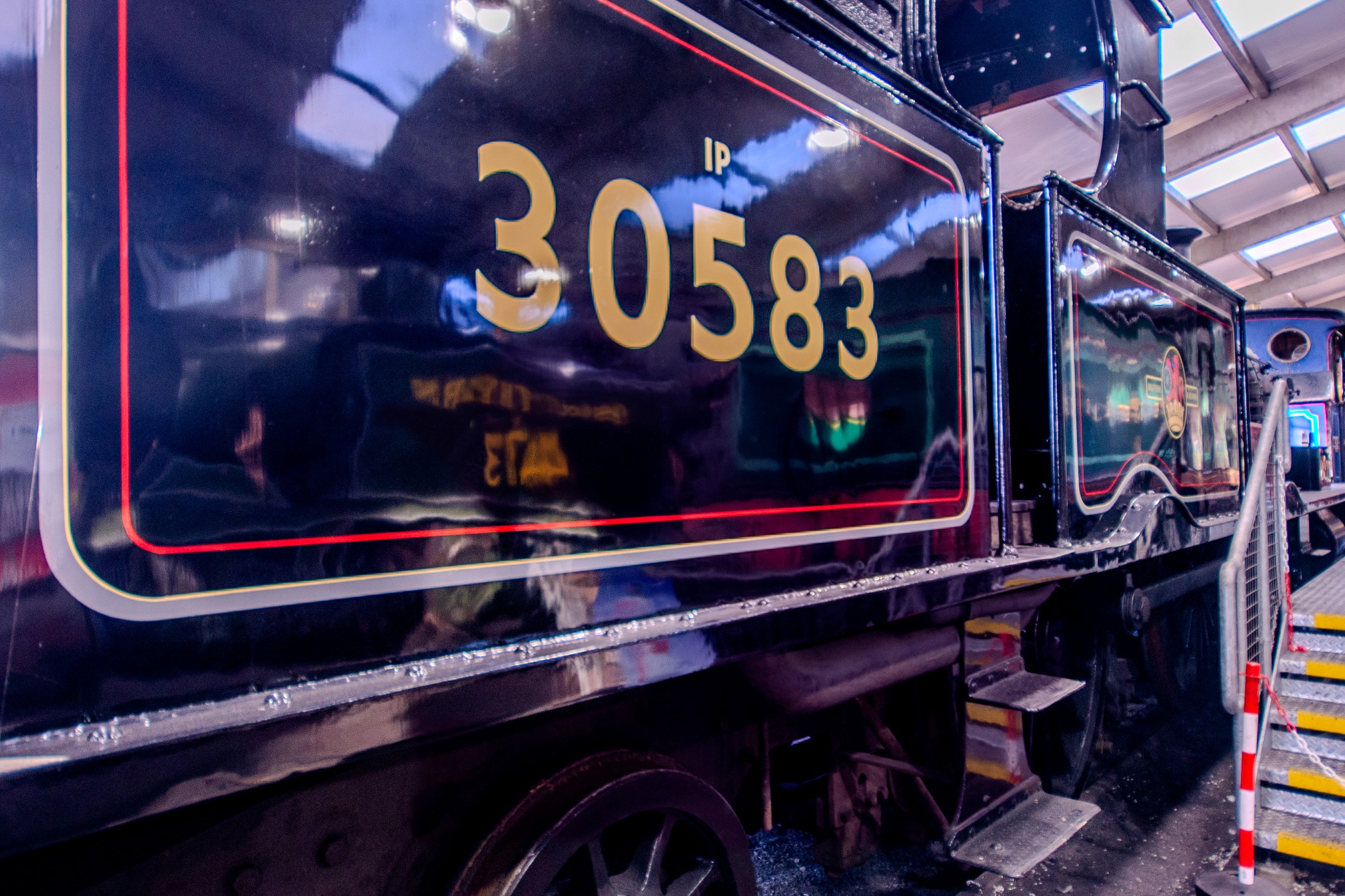 Steam locomotive cab interior showing pressure gauges, brass pipes, valves and a red regulator lever.